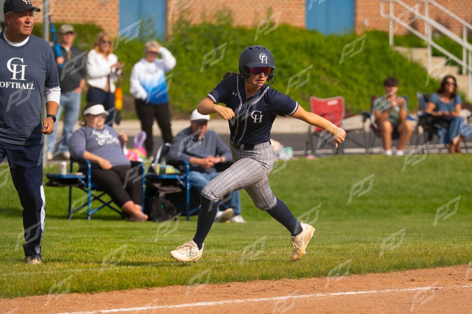 Softball player in navy pinstripe uniform rounds third base during a competitive game.