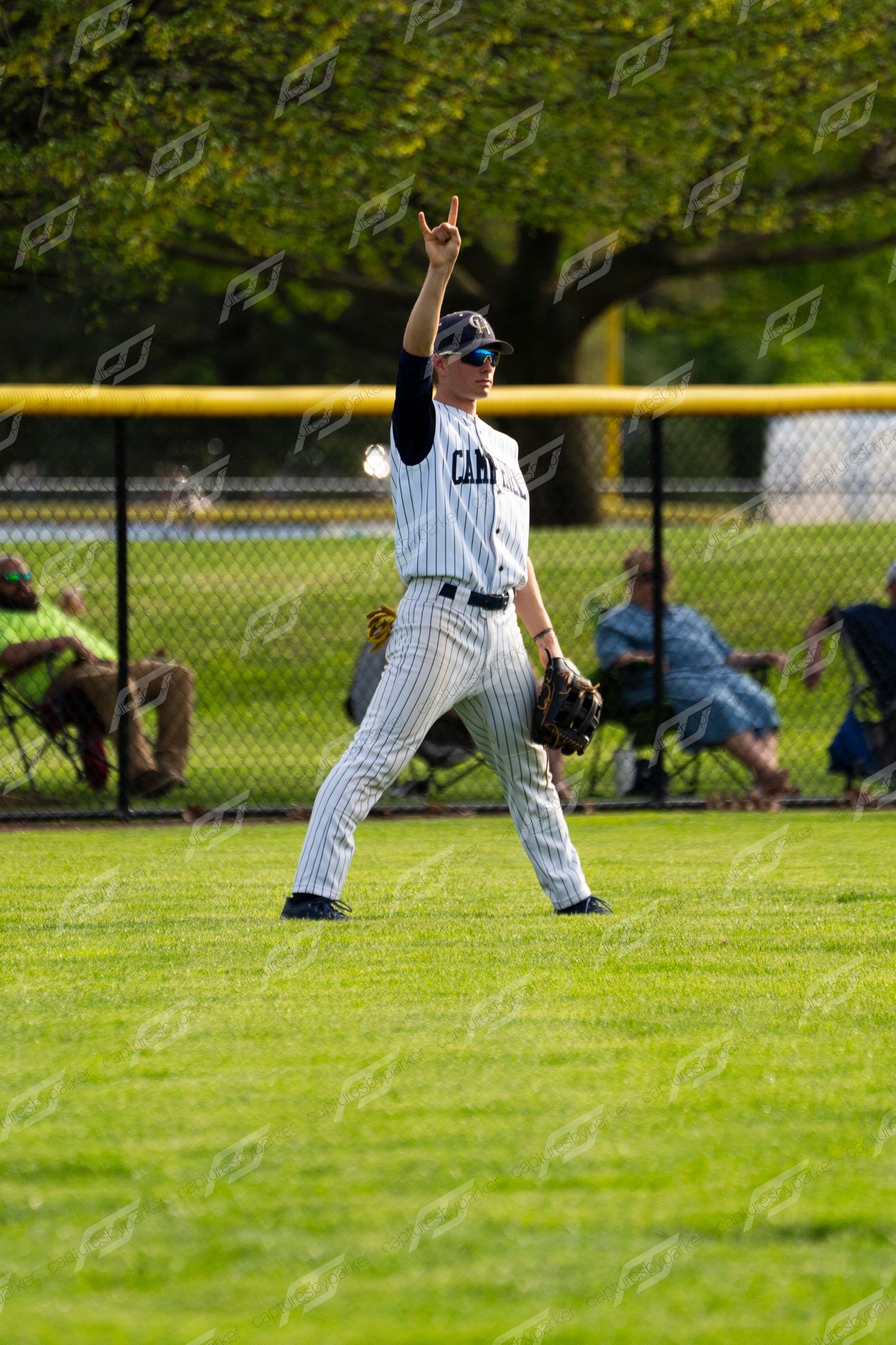 Camp Hill baseball outfielder in pinstripe uniform signaling with one finger raised while wearing sunglasses on the field.