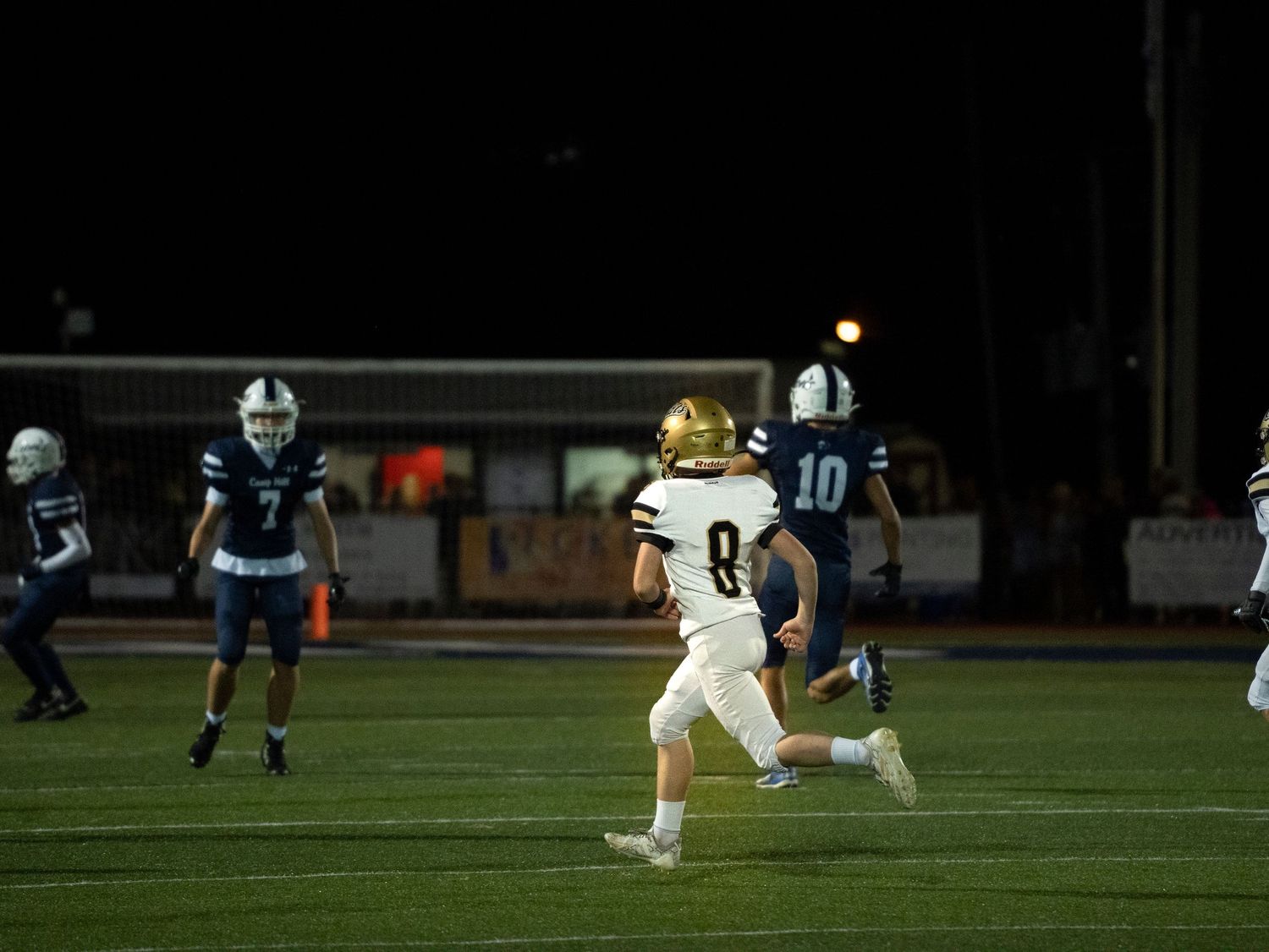 A Halifax high school football player wearing number 8 runs the ball during a night game against a blue-uniformed team.