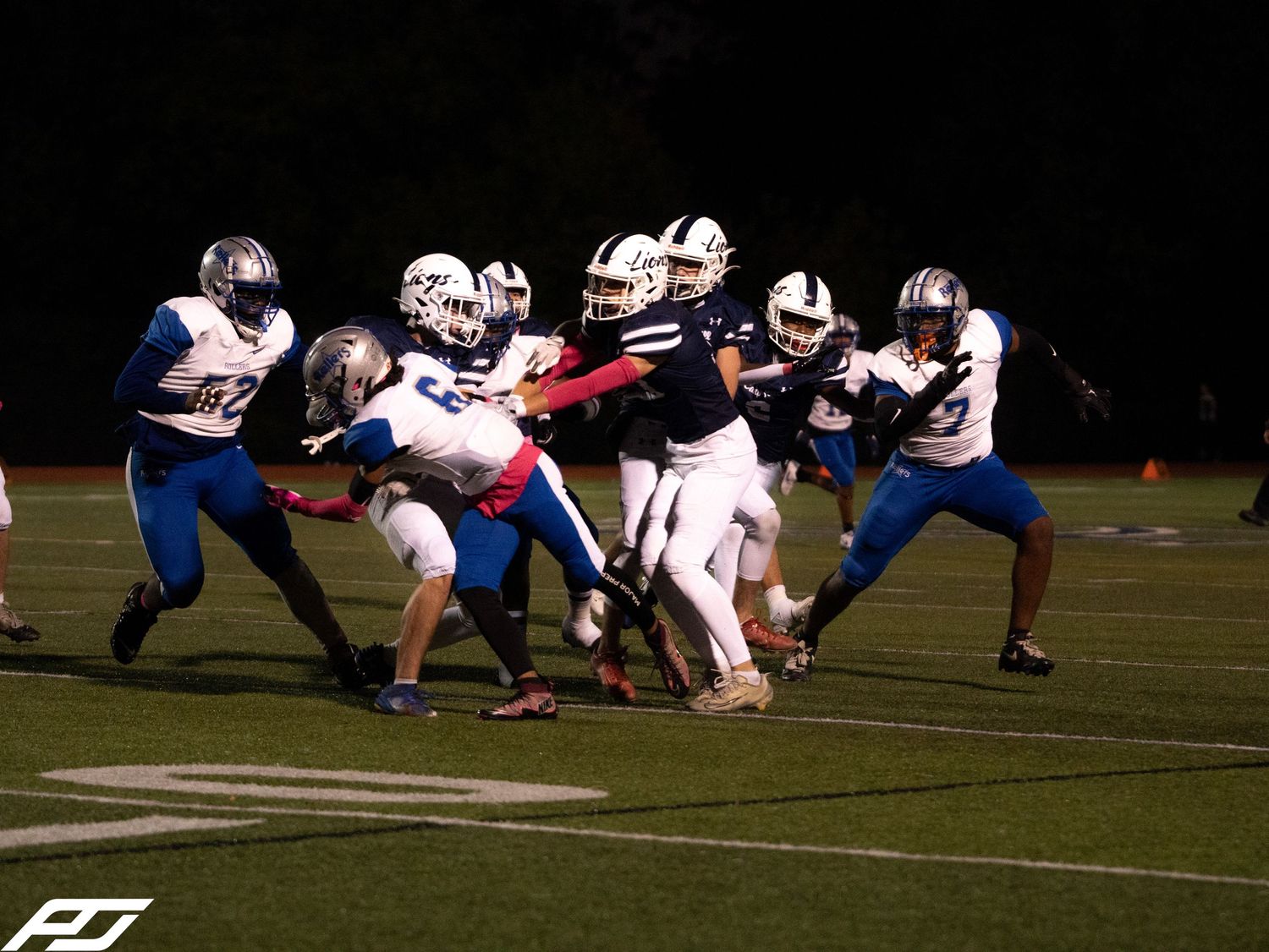 Camp Hill Lions football players engage in a tackle during an intense night game matchup.