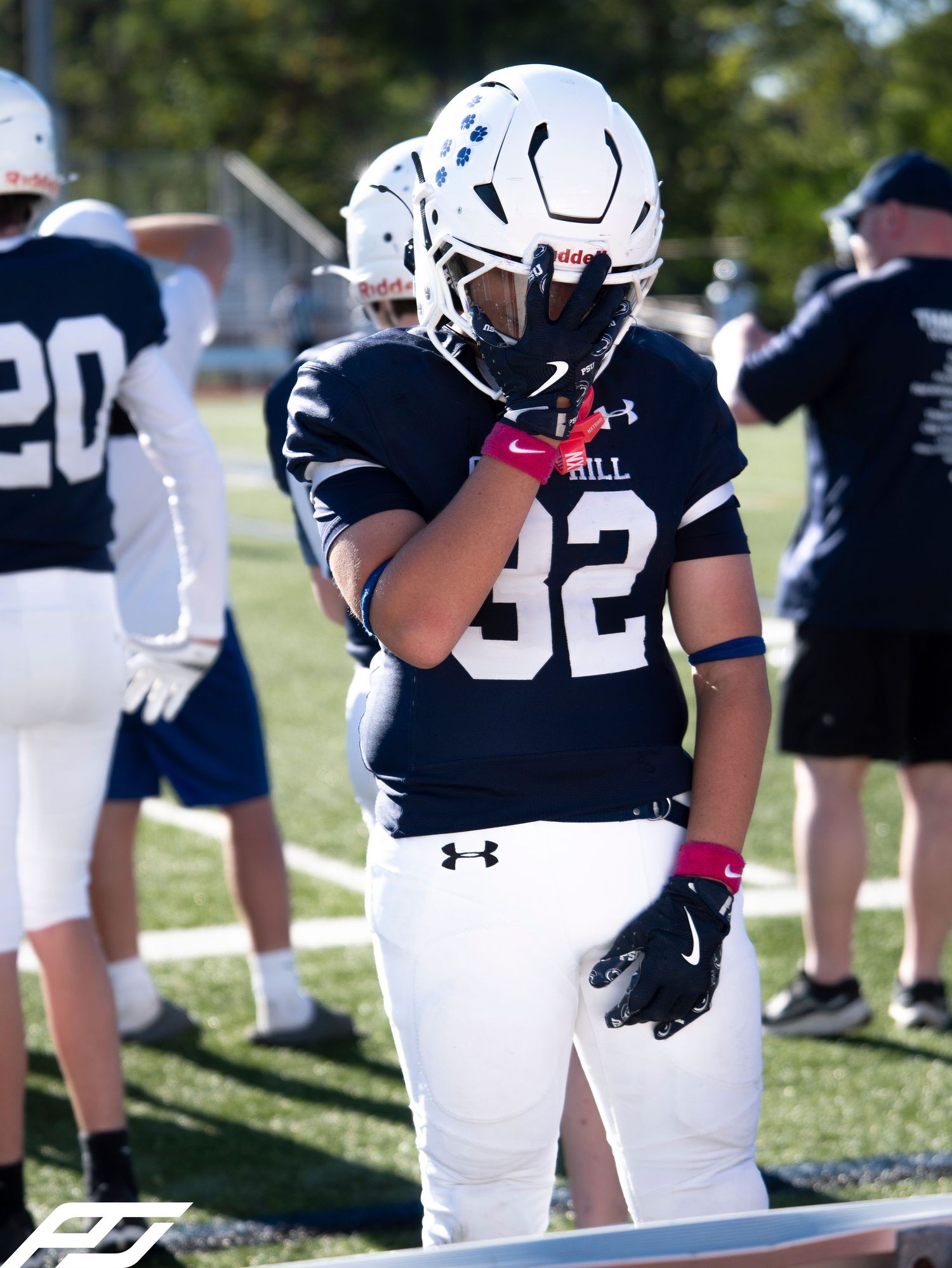 Football player wearing number 32 navy uniform adjusts gloves on sunny field.