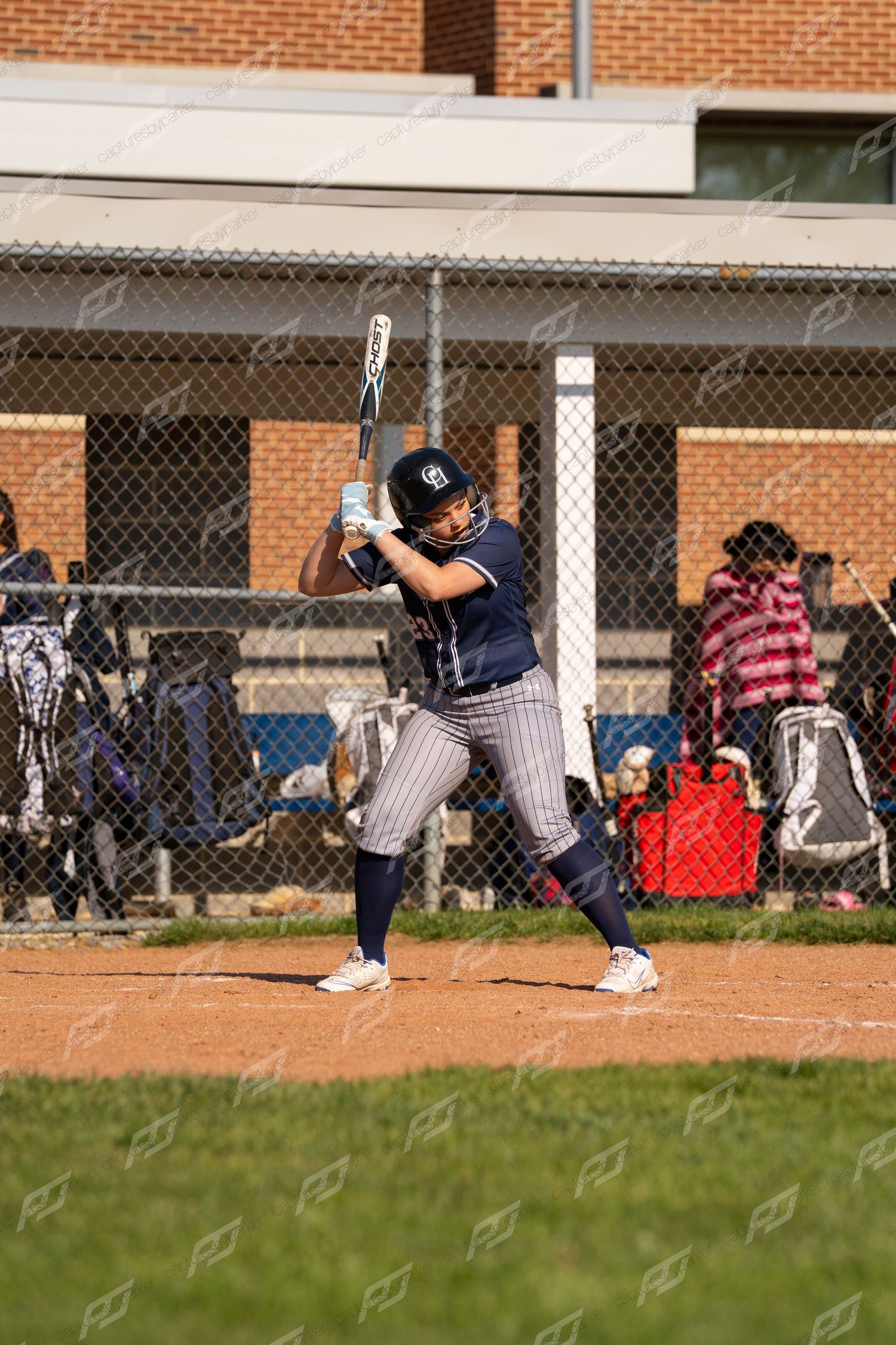 Female softball player in navy pinstripe uniform in batting stance preparing to hit during a game.