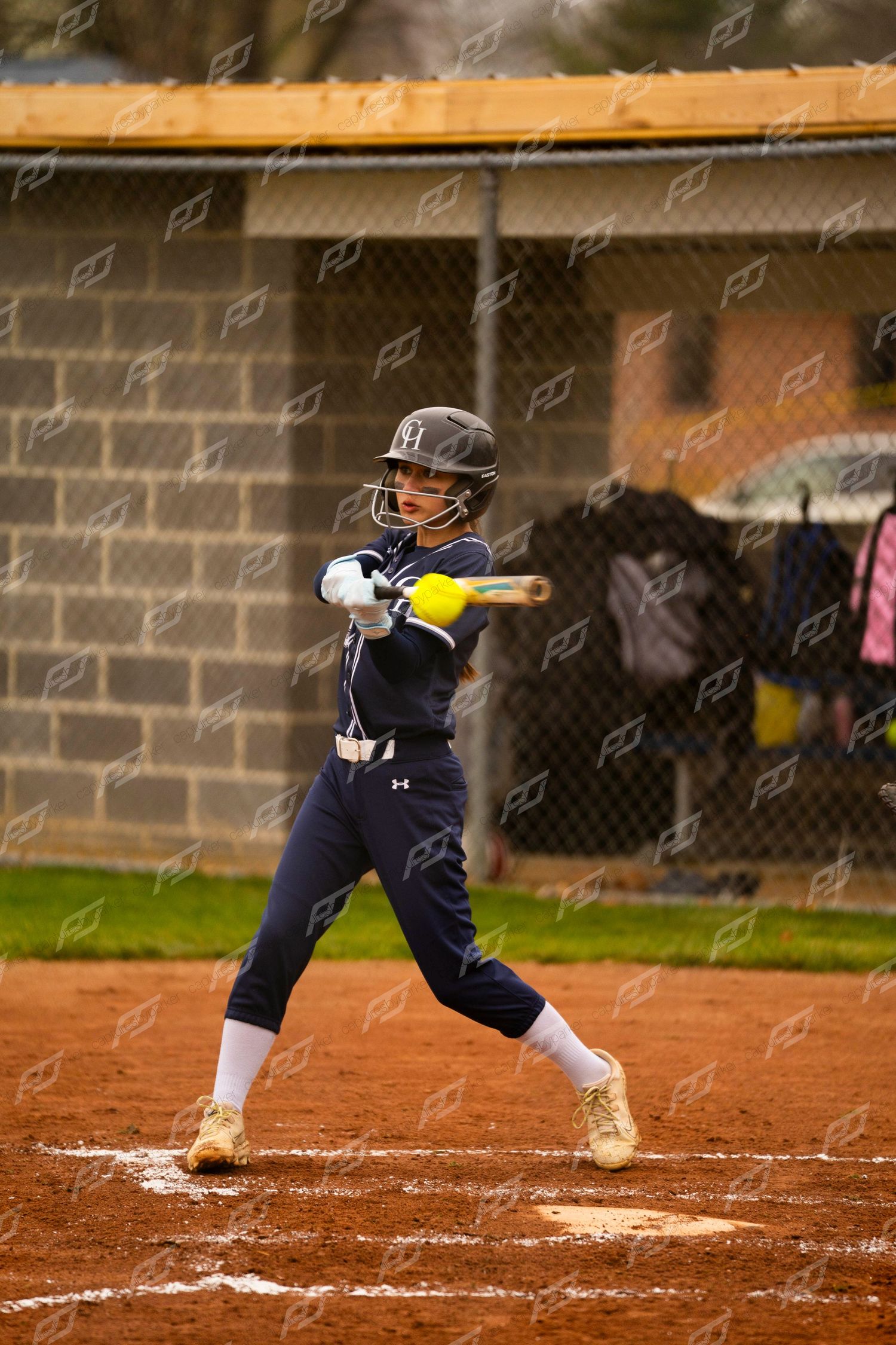 Young female softball player in navy Under Armour uniform follows through on a swing.