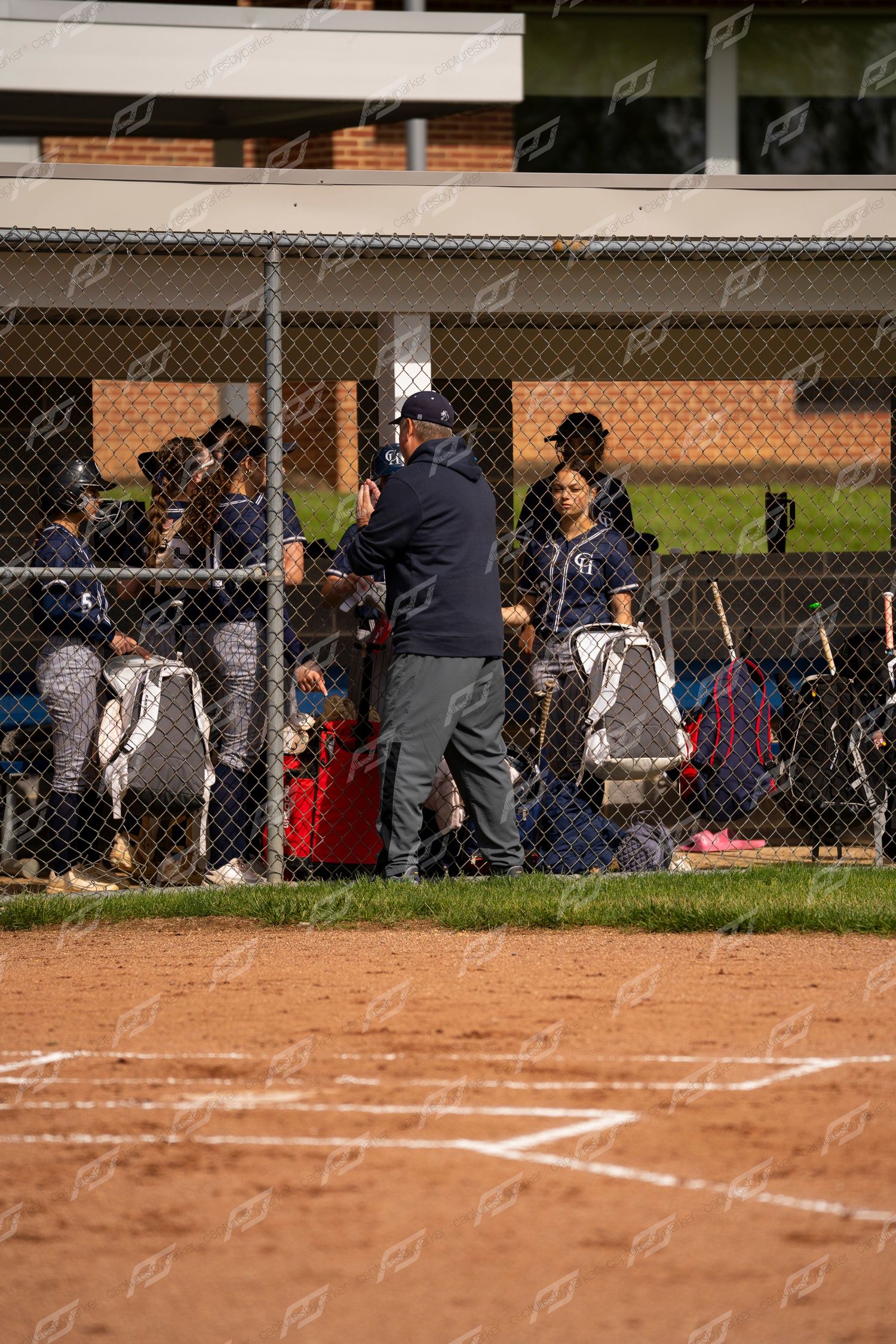 Softball coach talks to player through chain-link fence dugout during a game.