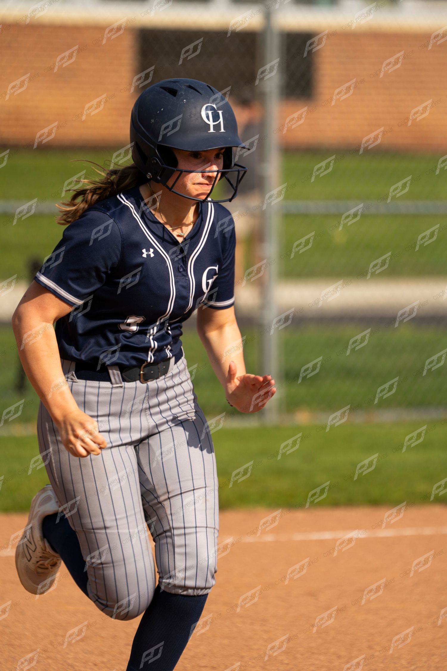 Female softball player wearing navy CH helmet and pinstripe uniform runs bases during game.