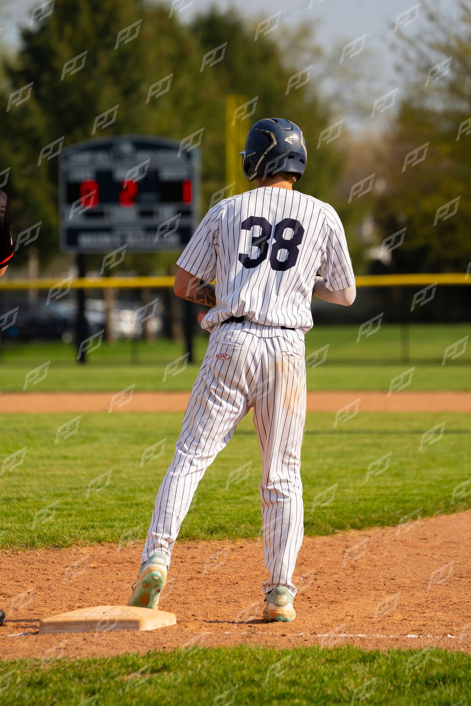 Baseball player #38 in white pinstripe uniform stands on base during an outdoor game.