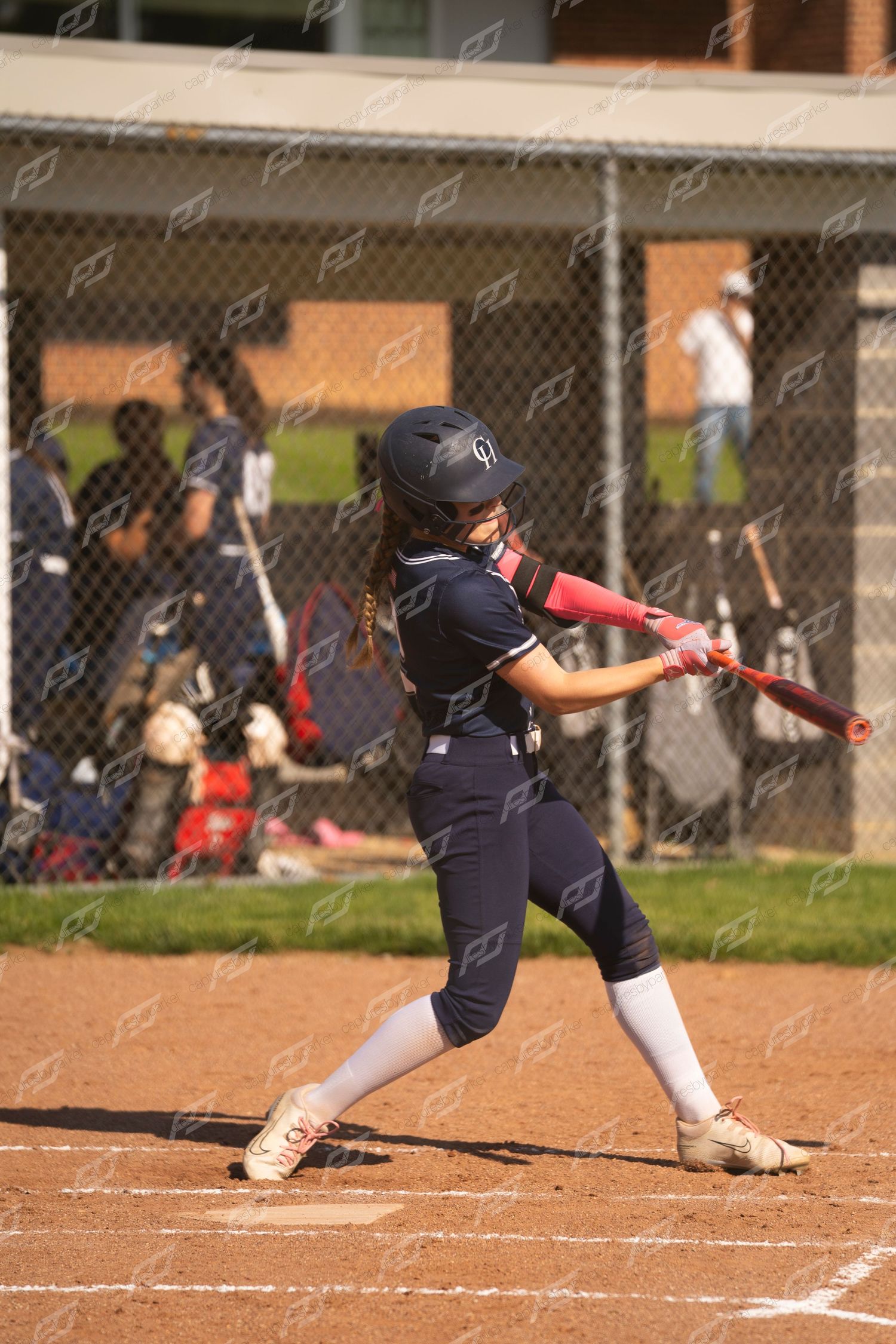 Young softball player in navy uniform swinging a pink bat at home plate during a game.