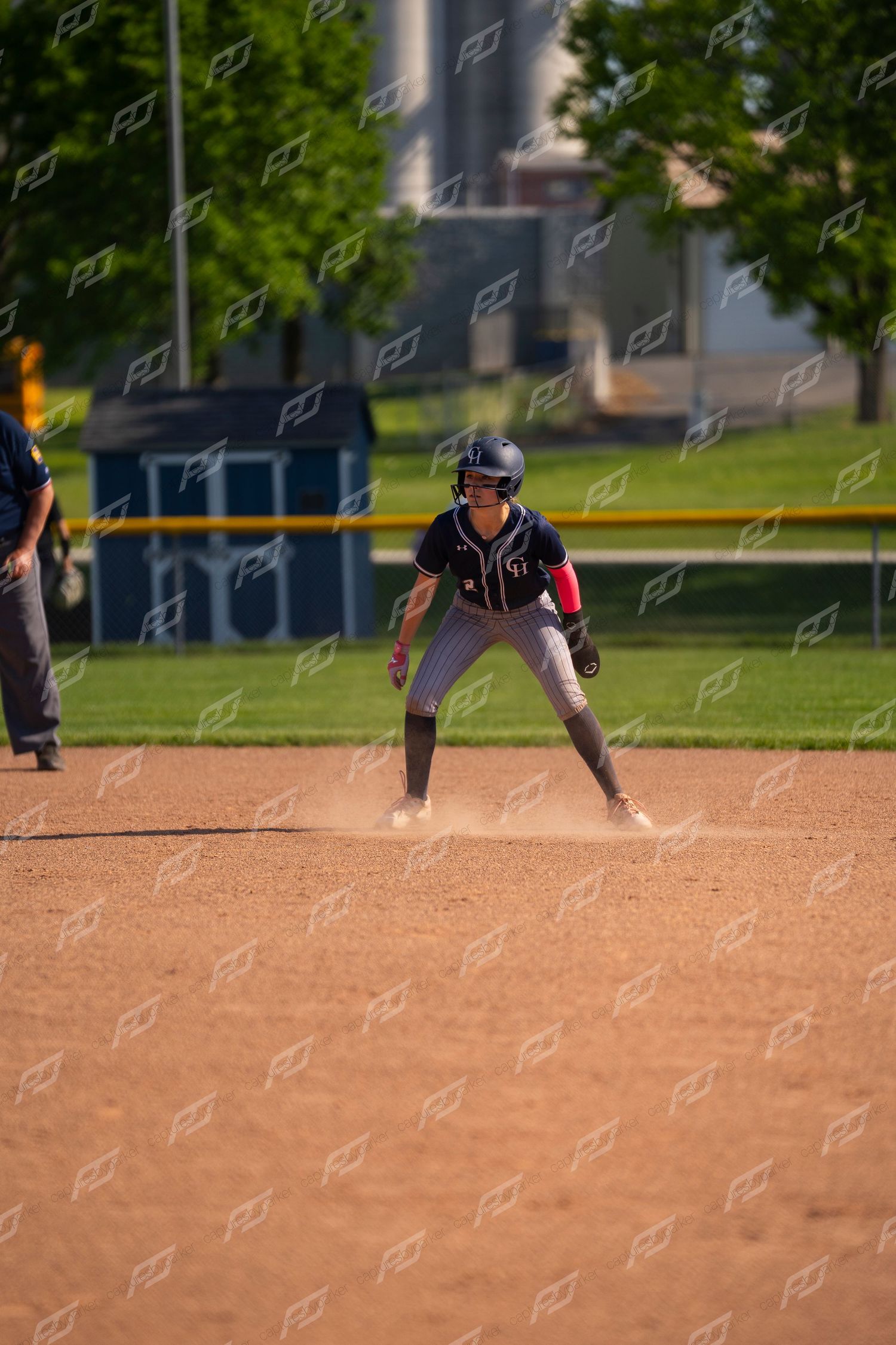 Softball player in navy uniform leads off second base during a sunny outdoor game.