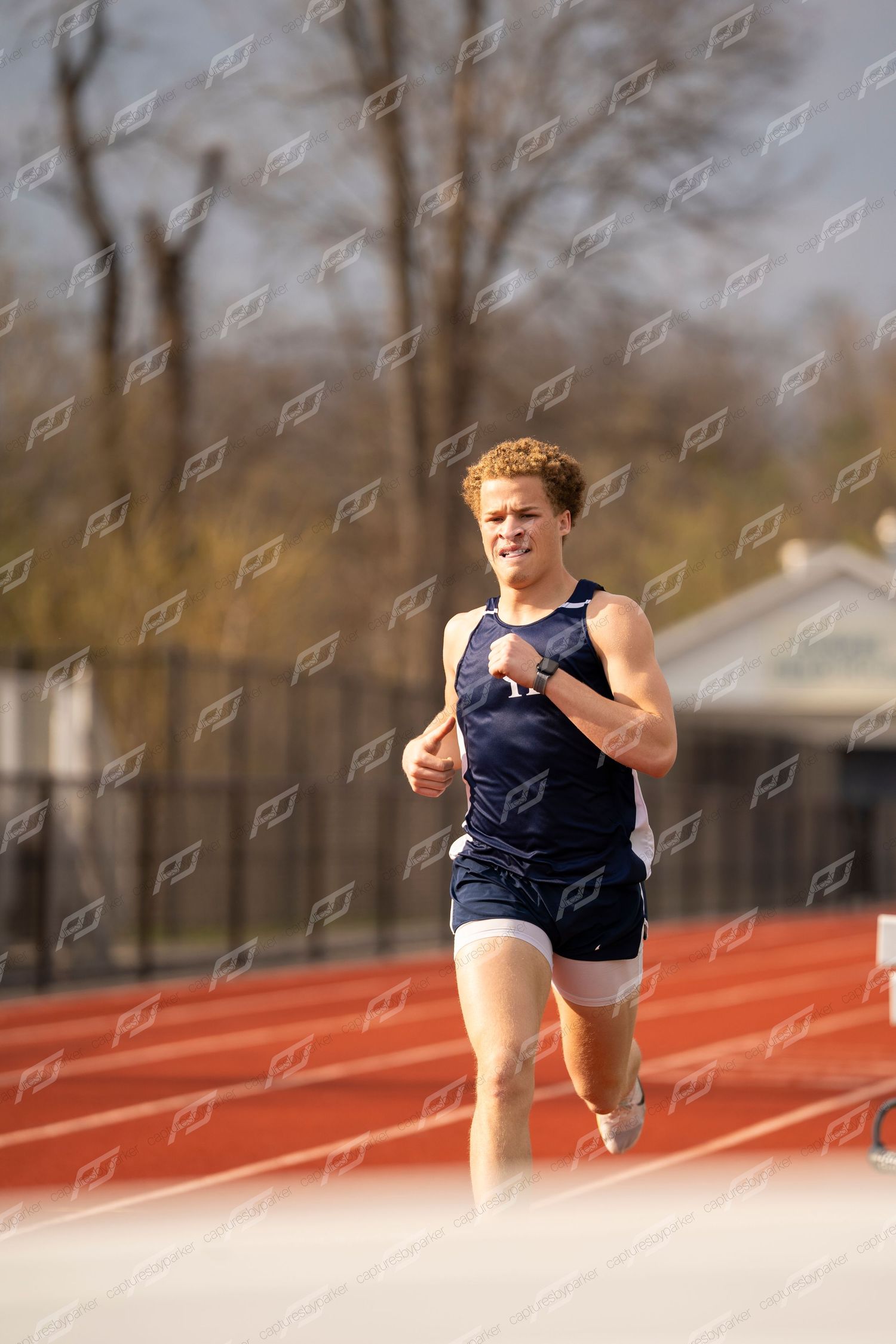 Male CH track runner in navy uniform sprinting on red track during race.