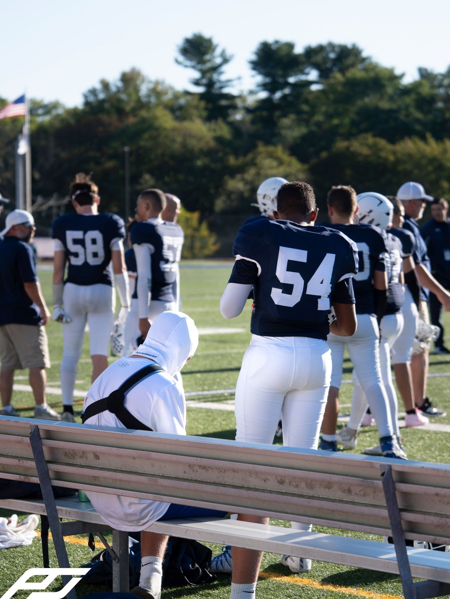 Camp Hill football players #54 and #58 stand on sideline watching game in navy uniforms.