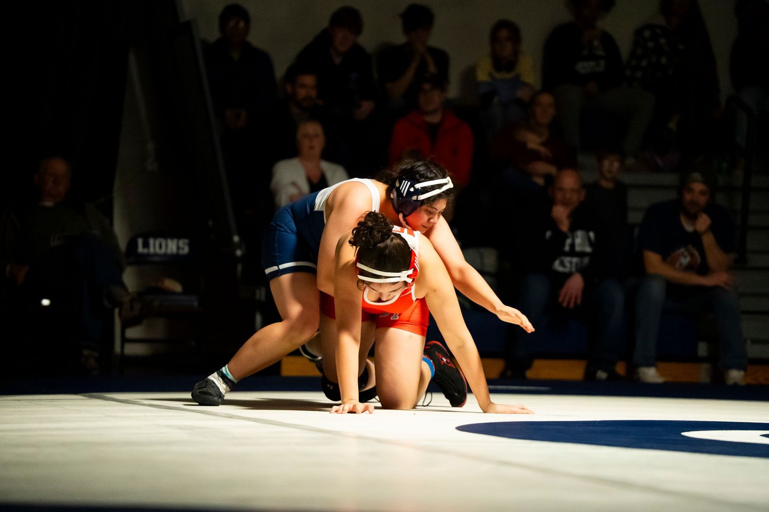 Two wrestlers compete on a blue mat during a high school wrestling match.