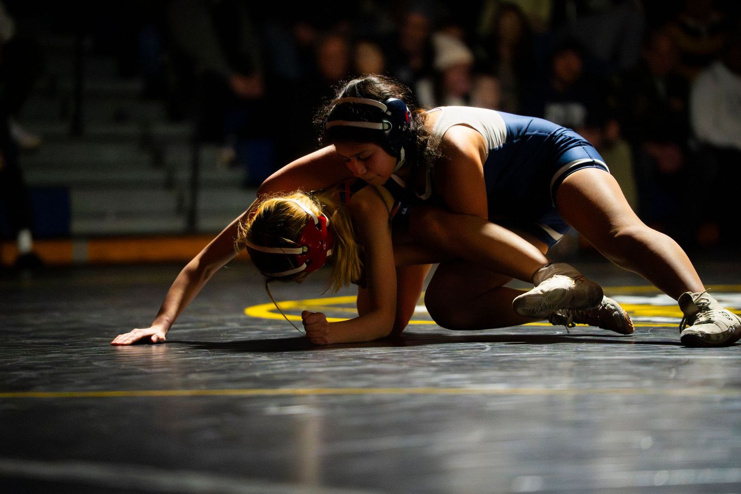 Female wrestler in blue singlet controls opponent during competitive wrestling match.