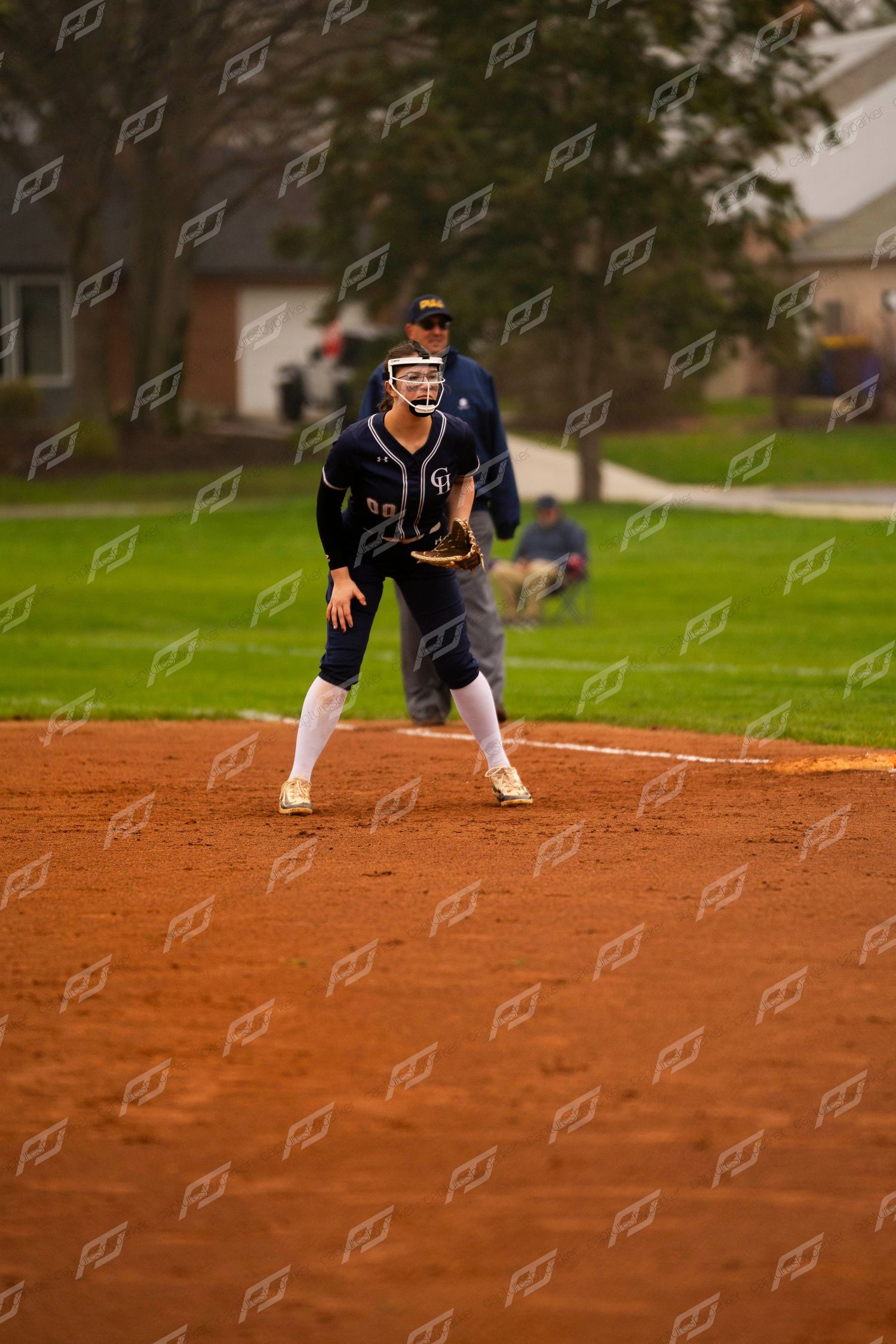 Female softball infielder in navy CH uniform crouches in ready position on field.