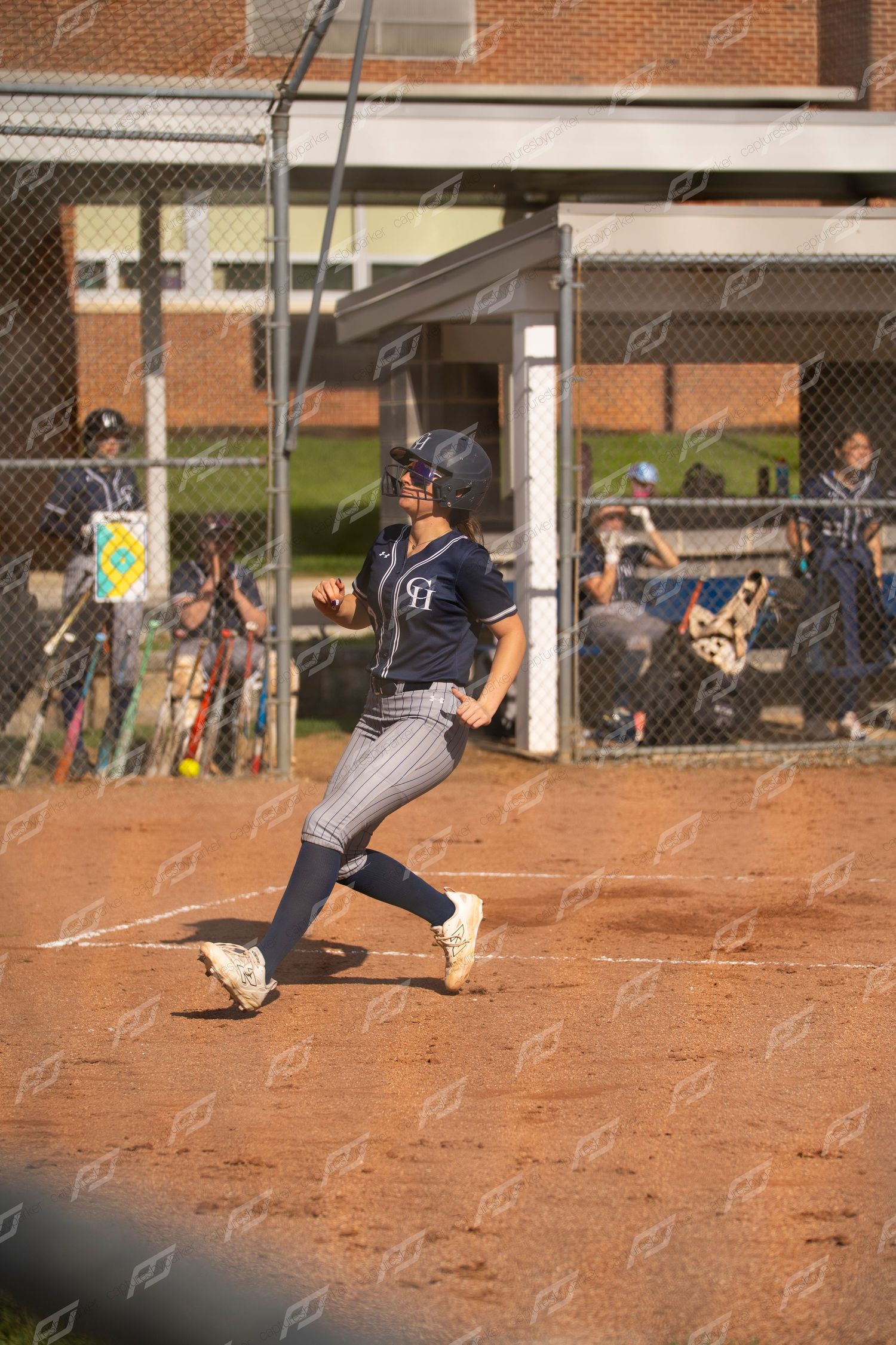 Female softball player in navy uniform runs toward home plate during a softball game.