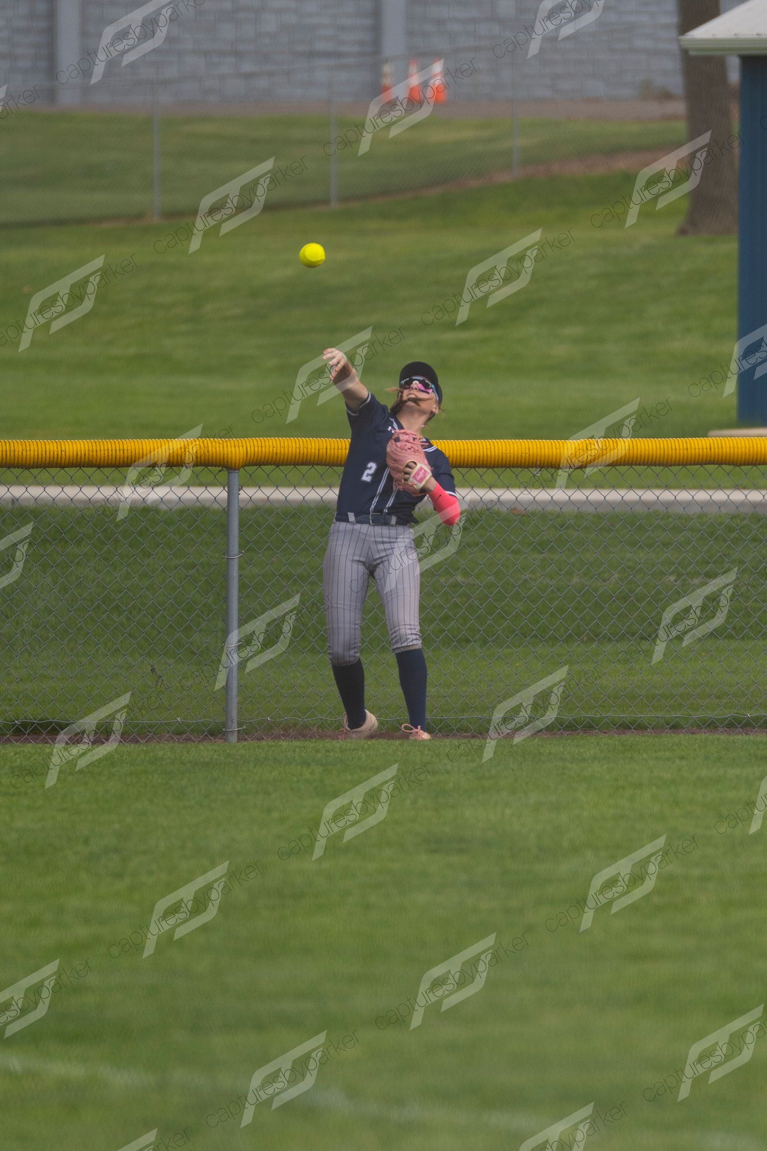 Softball outfielder #2 in navy uniform throws a yellow ball across the field.