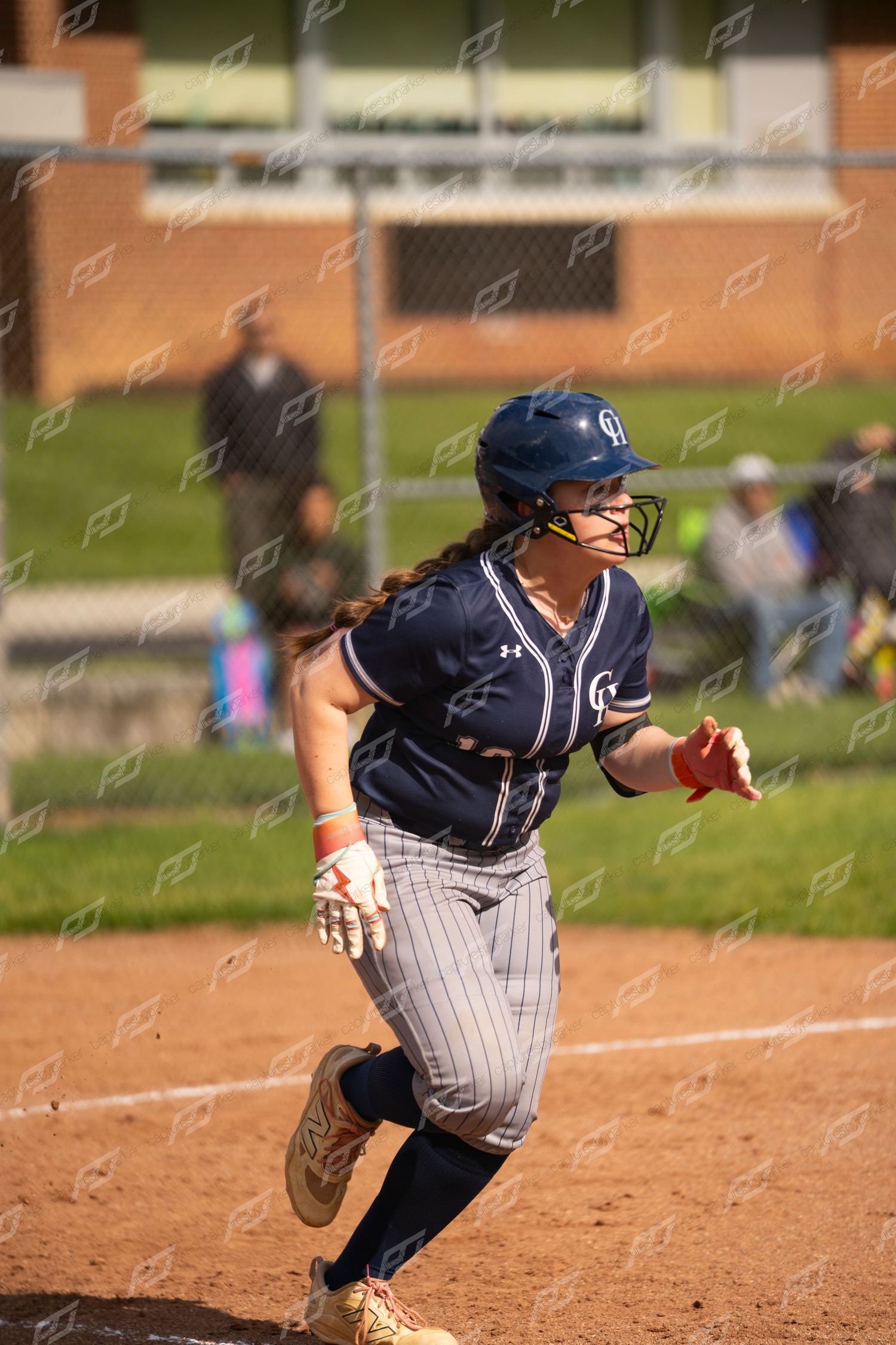 Female softball player in navy uniform sprints from home plate during outdoor game.