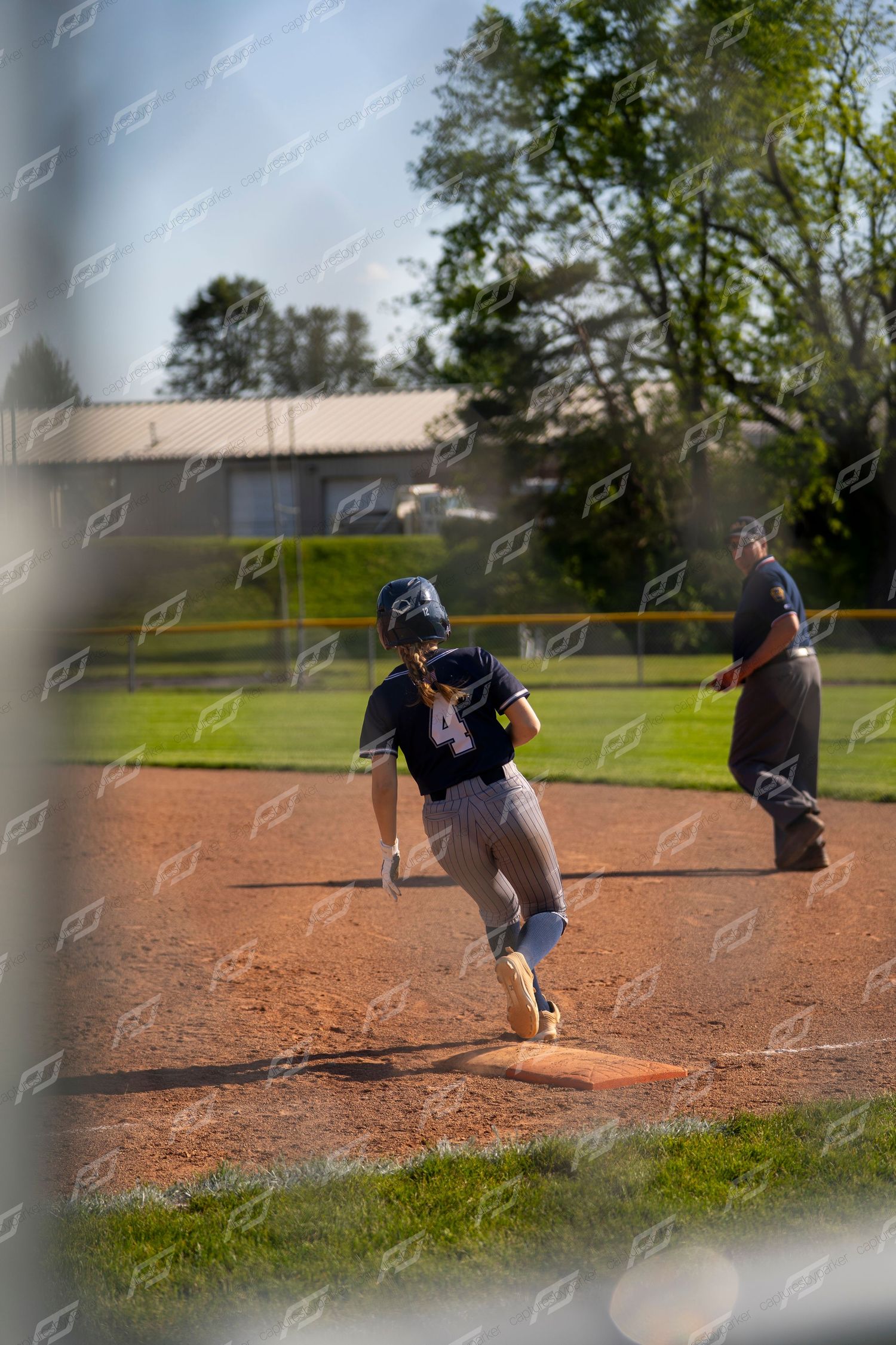 Female softball player number 4 rounding a base with an umpire standing nearby.