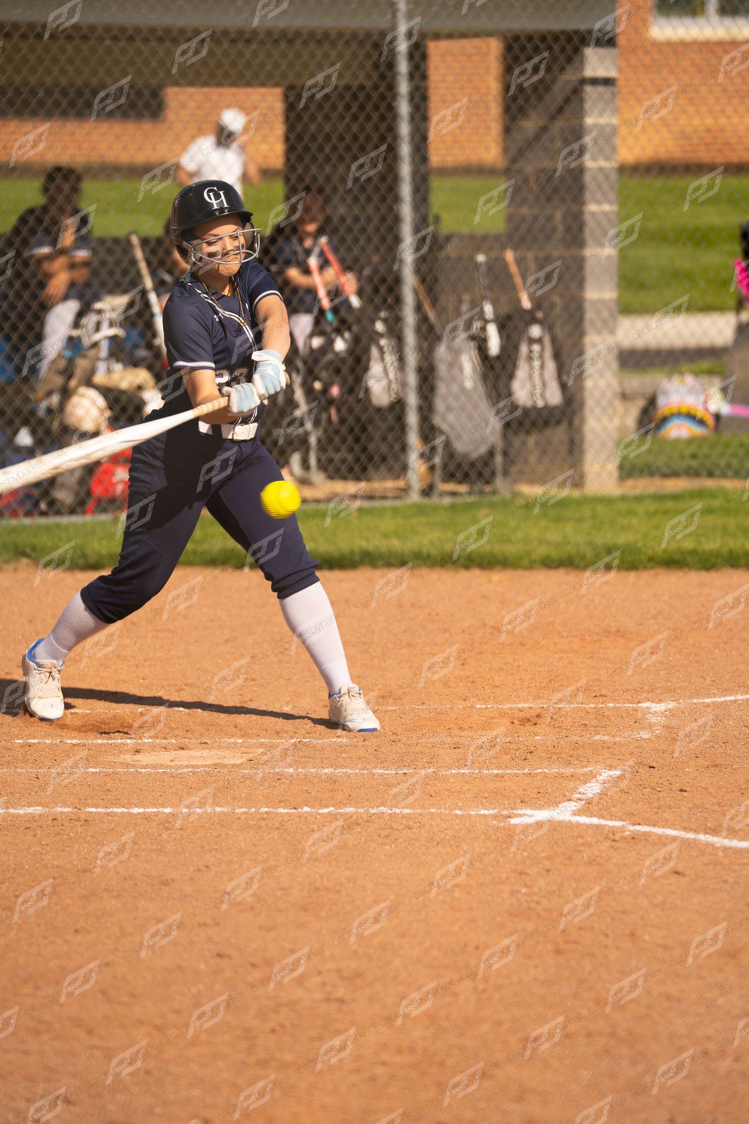 Female softball batter in navy uniform makes contact with yellow ball during game.