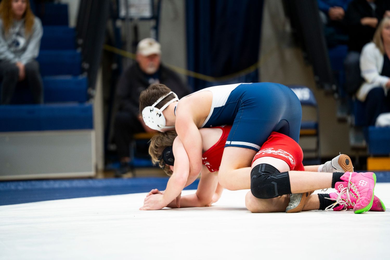 High school wrestler in blue singlet works to pin red-uniformed opponent during a wrestling match.
