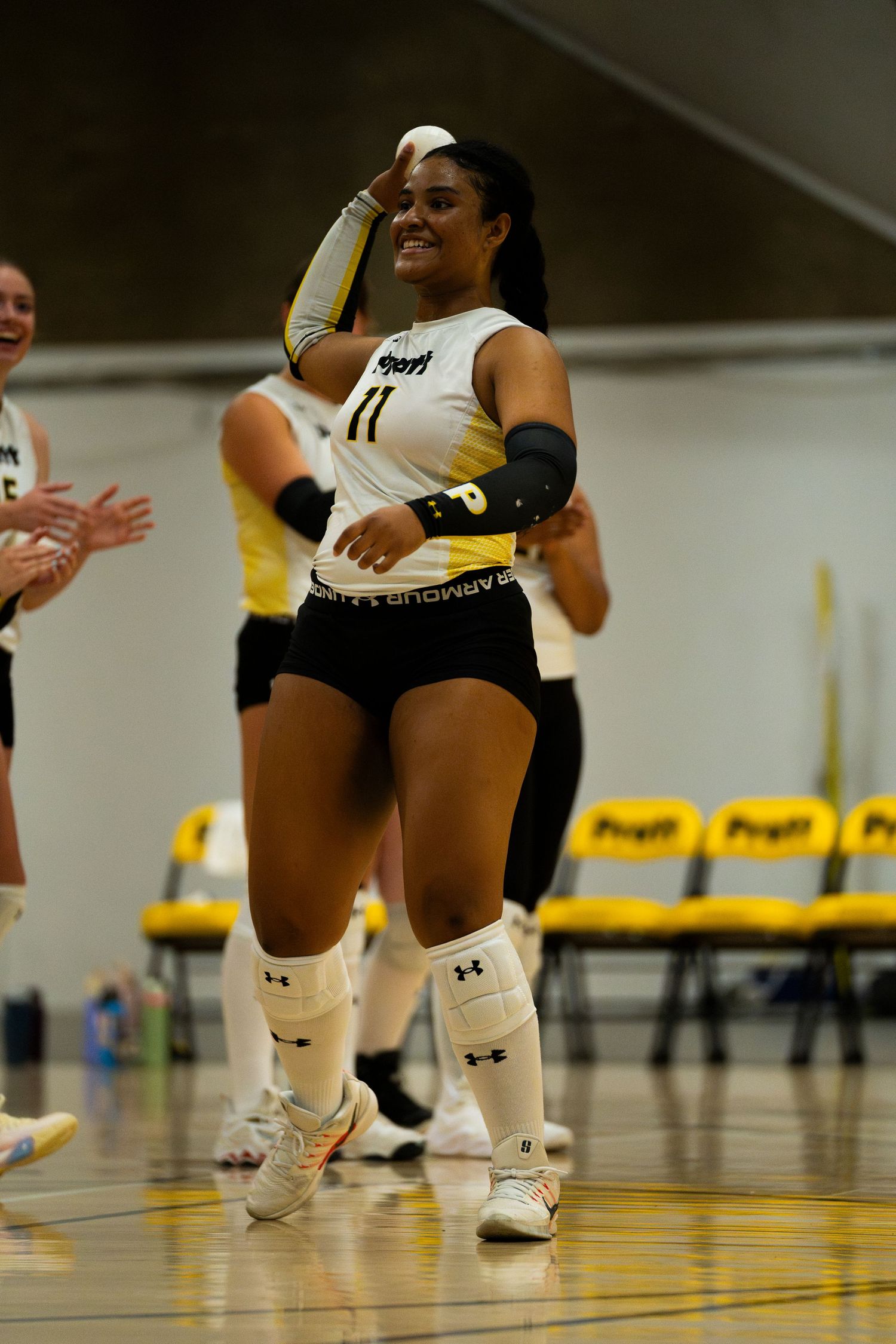 Smiling volleyball player #11 in black and white uniform with knee pads celebrates on indoor court.