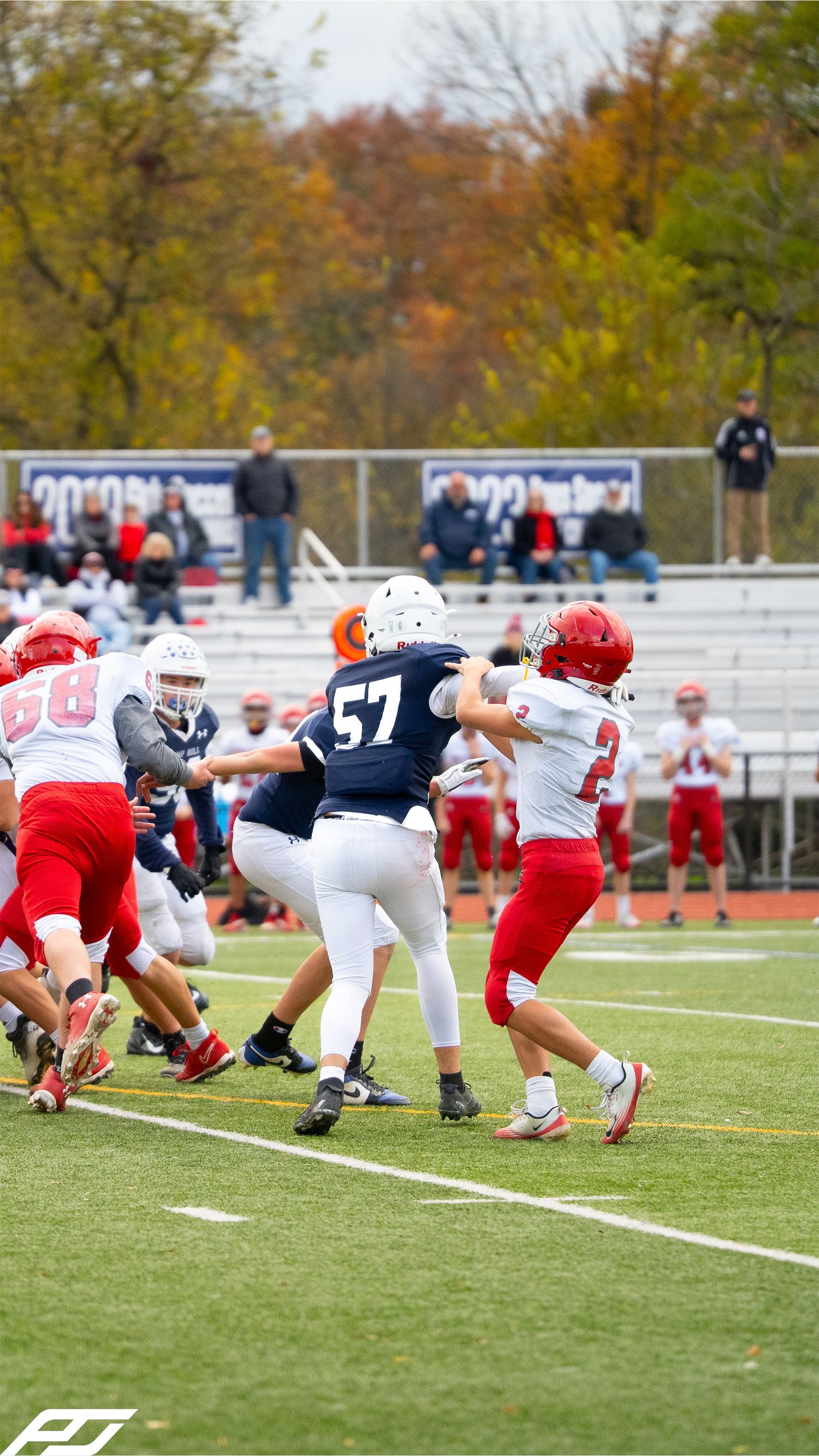 Youth football players in navy blue uniforms defend against red-uniformed opponents during a competitive game on turf.
