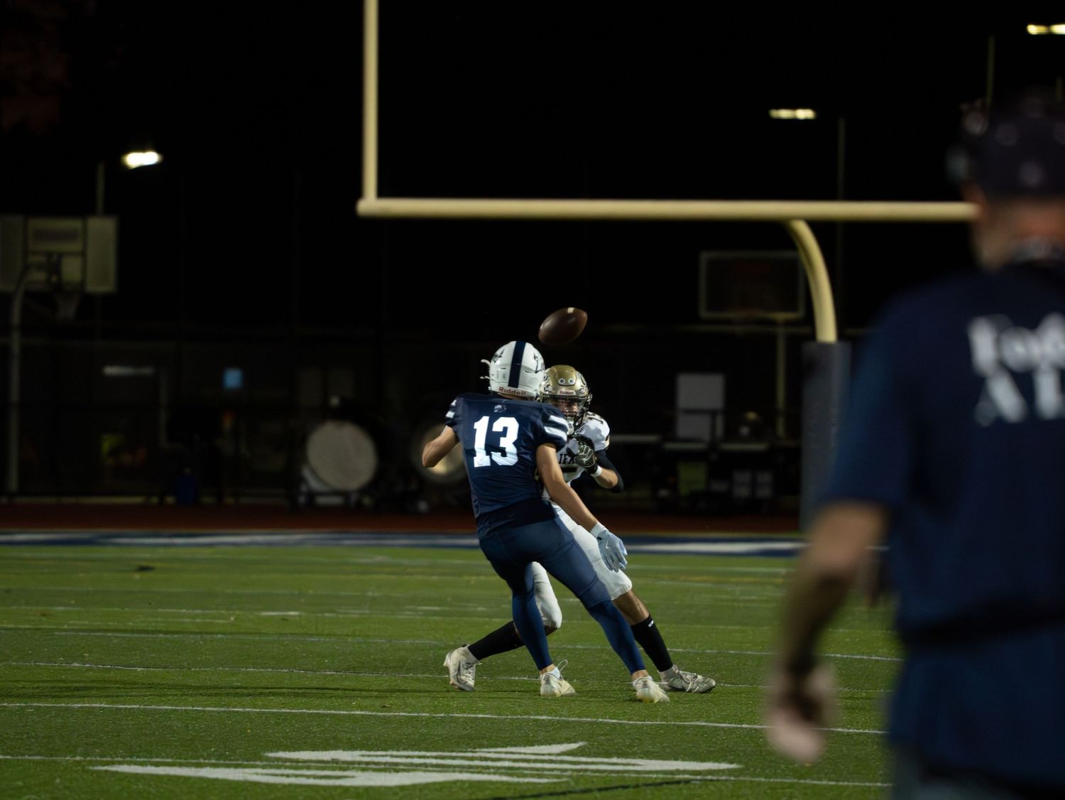 A high school football player wearing number 13 catches a pass during a night game on a well-lit football field.