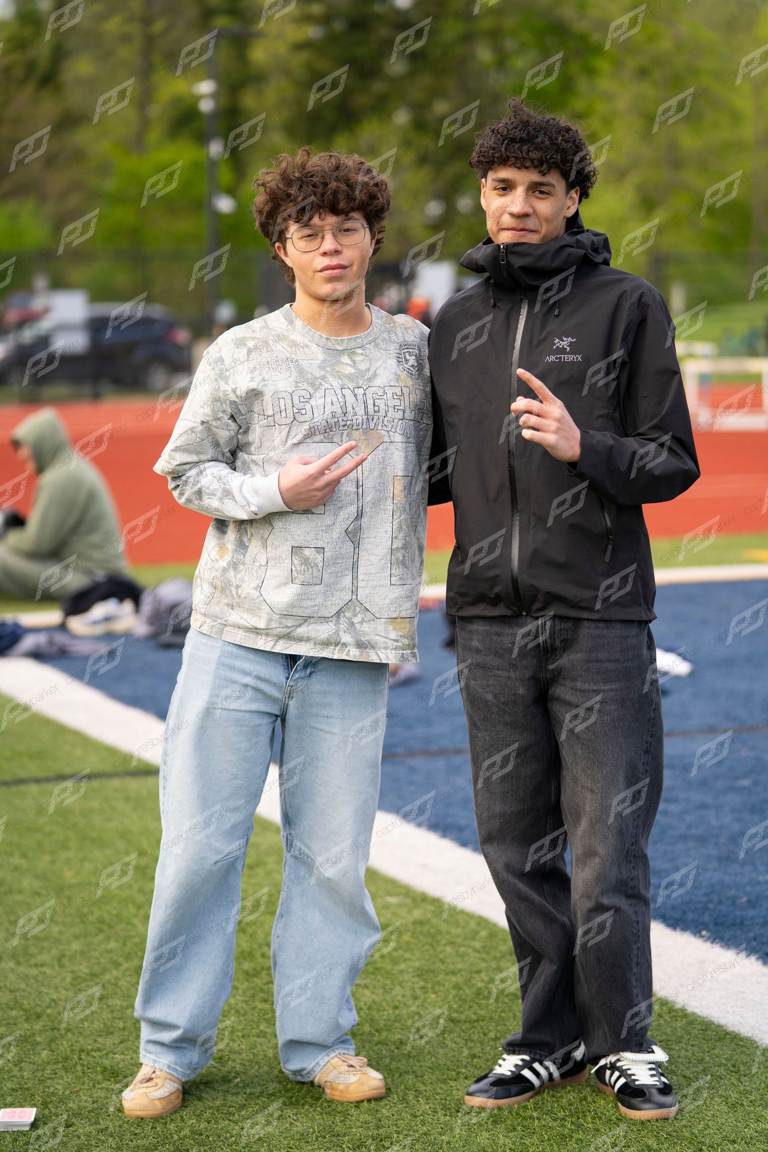 Two young male athletes pose together on football field sideline at outdoor track meet.