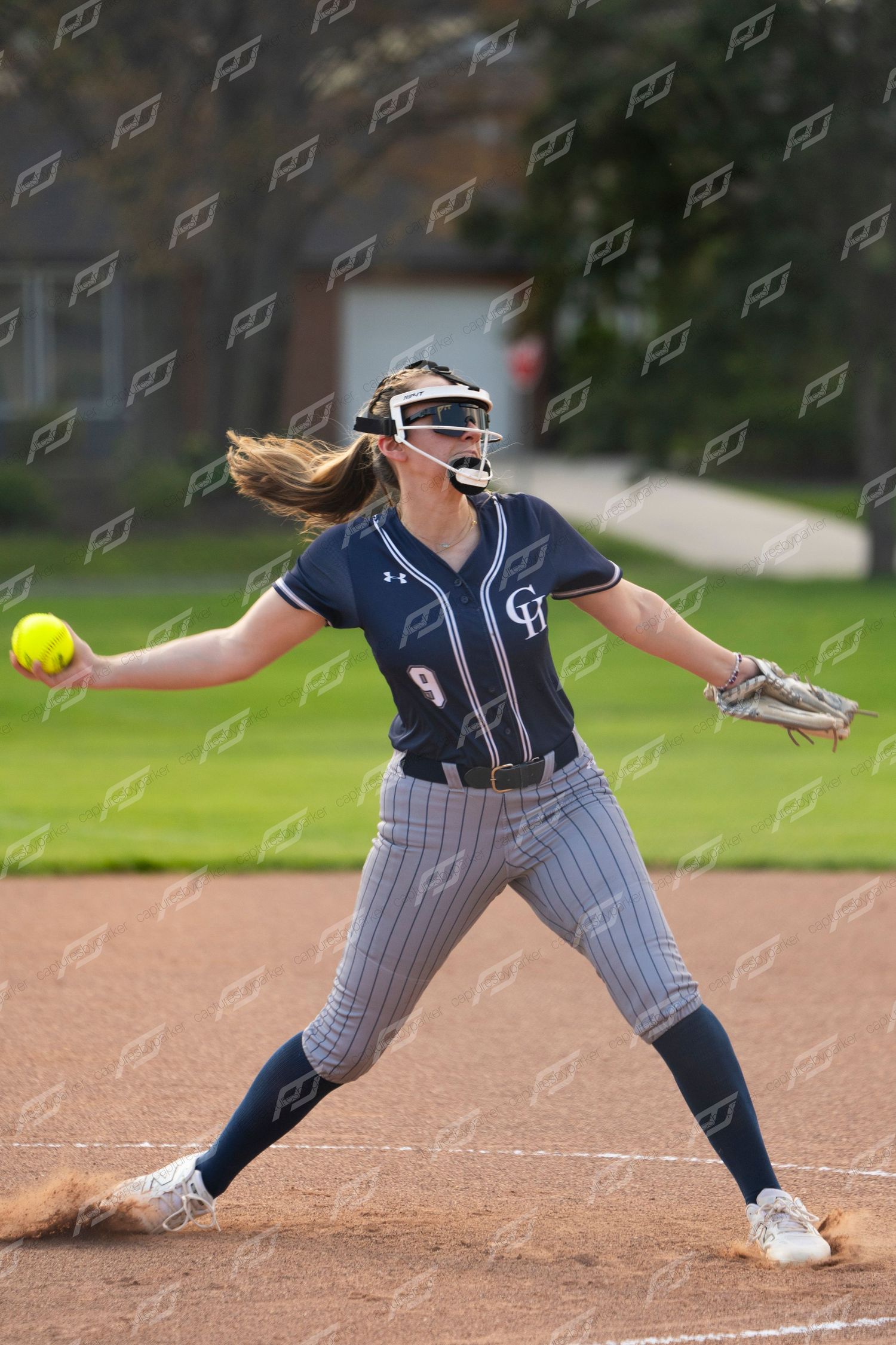 Female softball pitcher number 9 winds up to throw a yellow ball during a game.