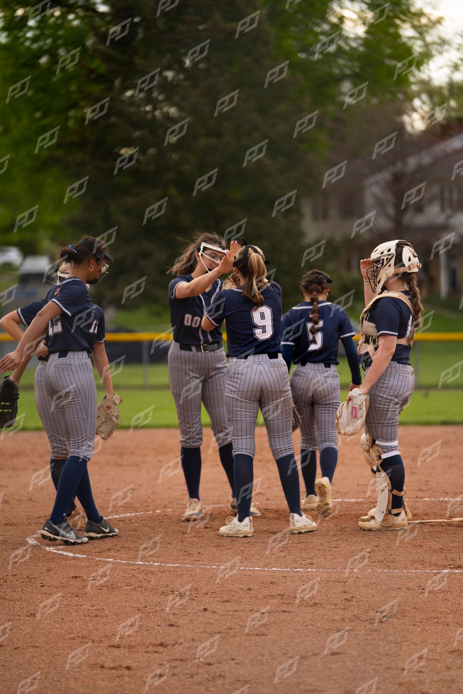 Softball team gathers on the pitcher's mound for a celebratory huddle during a game.