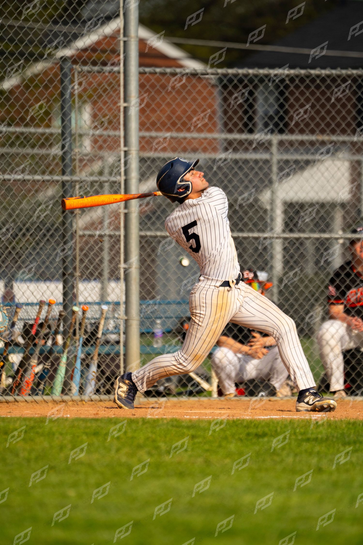 Baseball player number 5 in pinstripe uniform making powerful contact with the baseball.