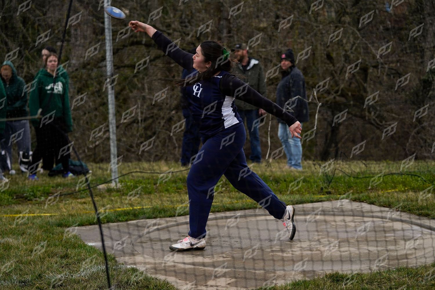 Female athlete in navy uniform throwing discus at an outdoor track and field competition.
