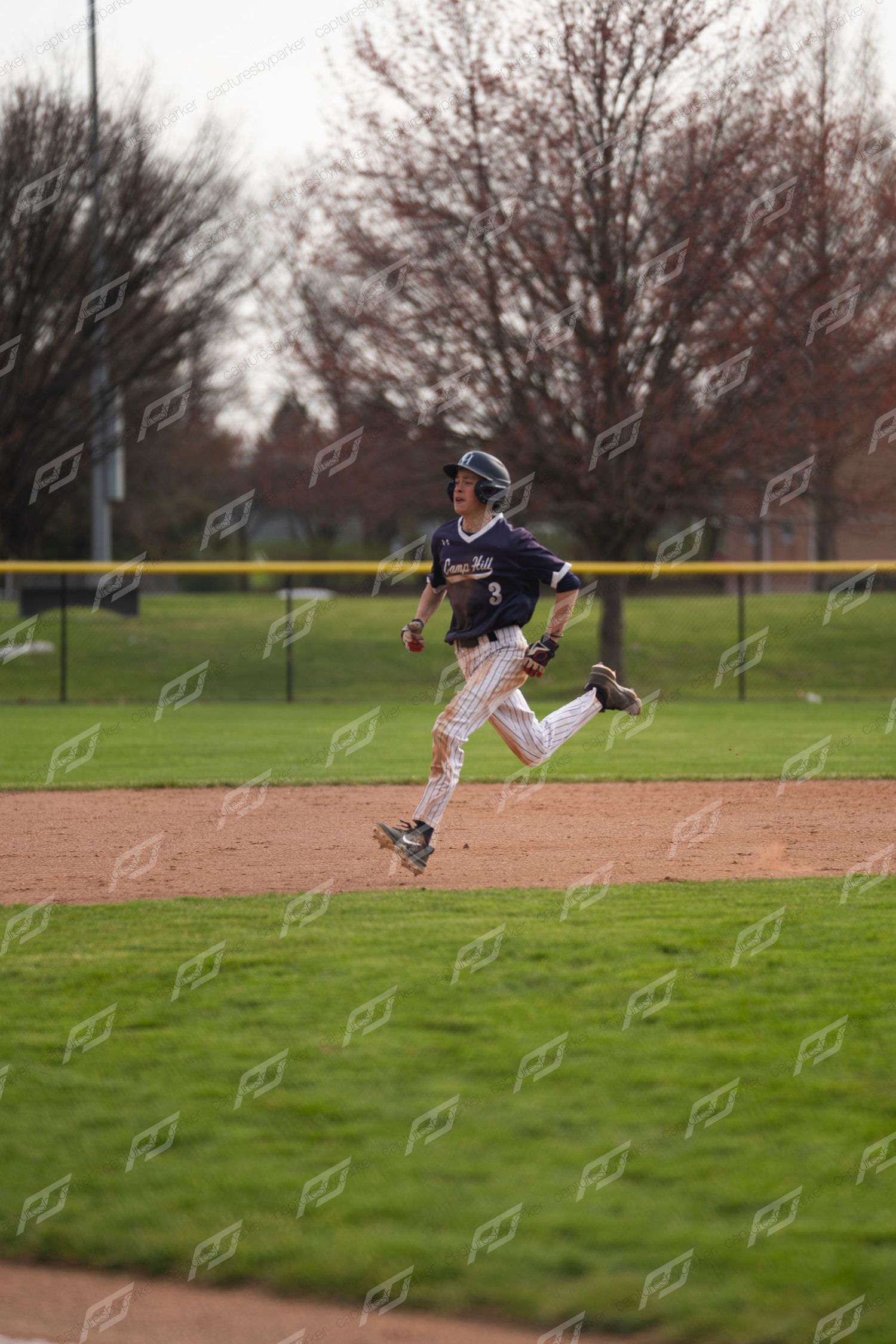 Baseball player #3 sprints along the baseline during a youth baseball game on a green field.