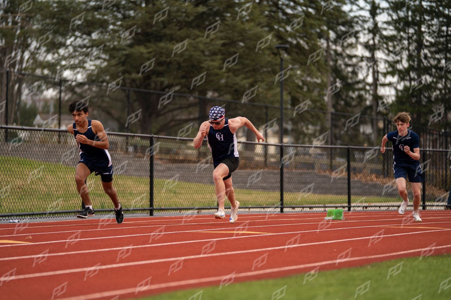 Three male athletes sprint down red track during competitive track meet.