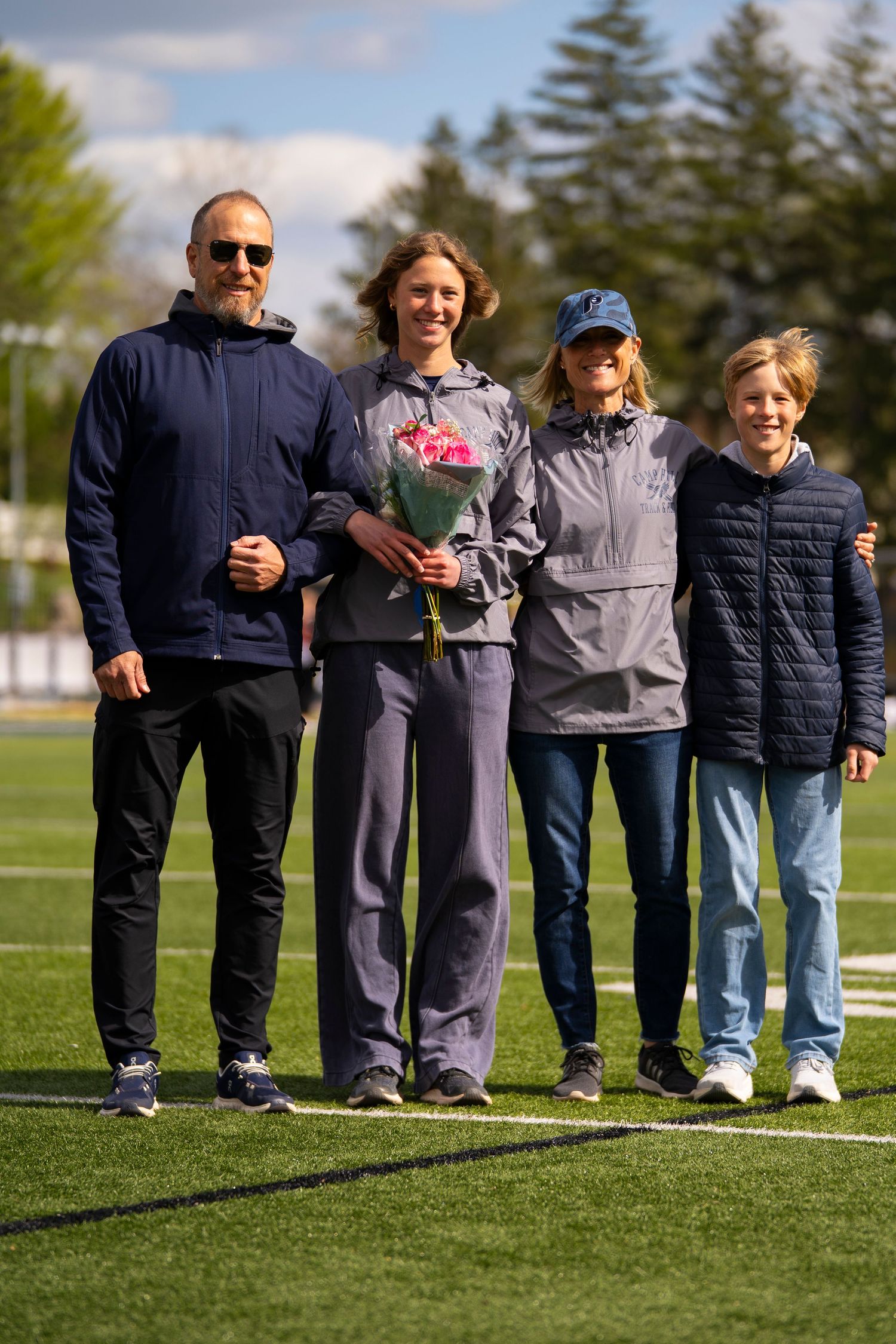 A family of four poses on a football field during a spring senior day ceremony.