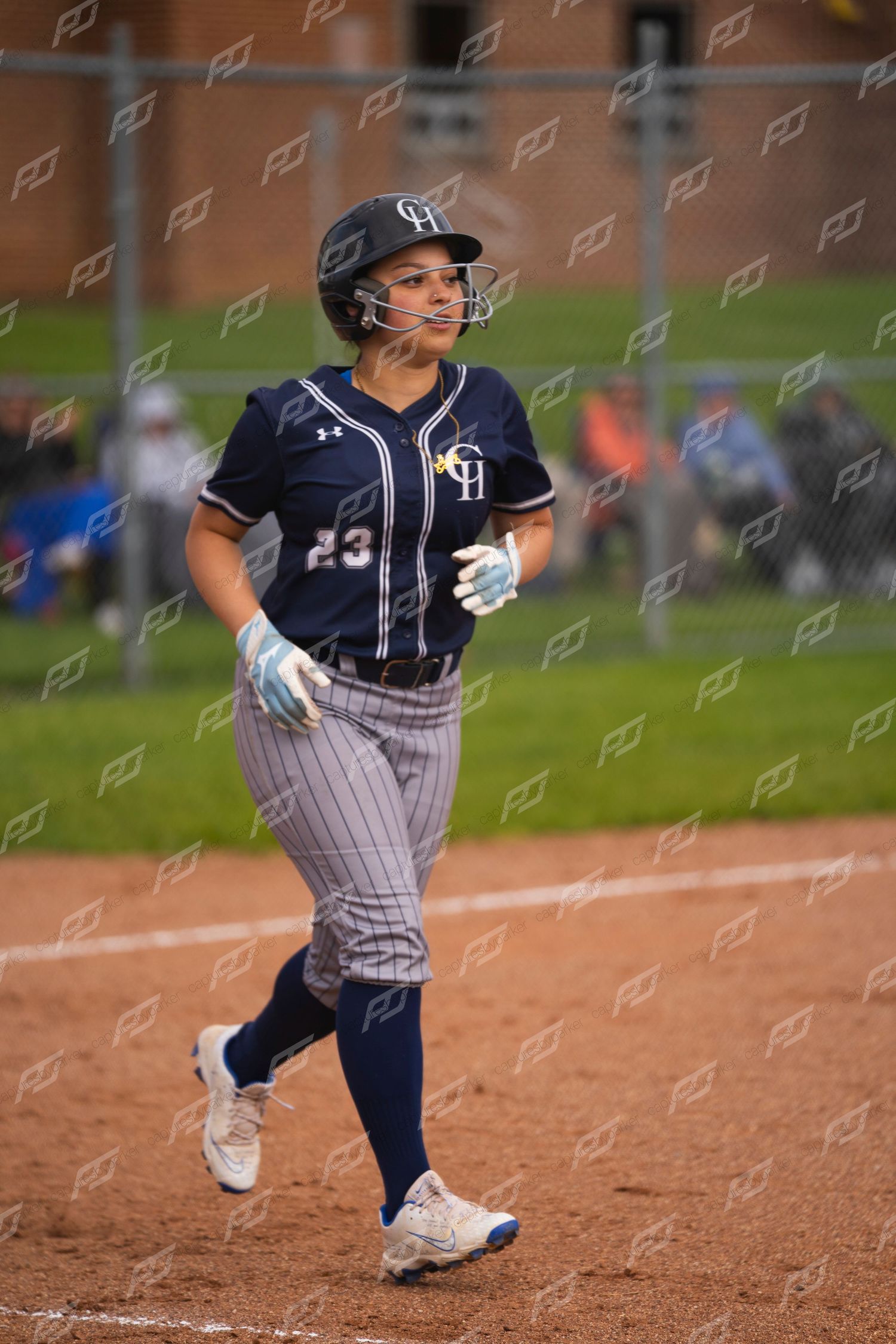 Female softball player number 23 in navy GH uniform jogs bases during outdoor game.