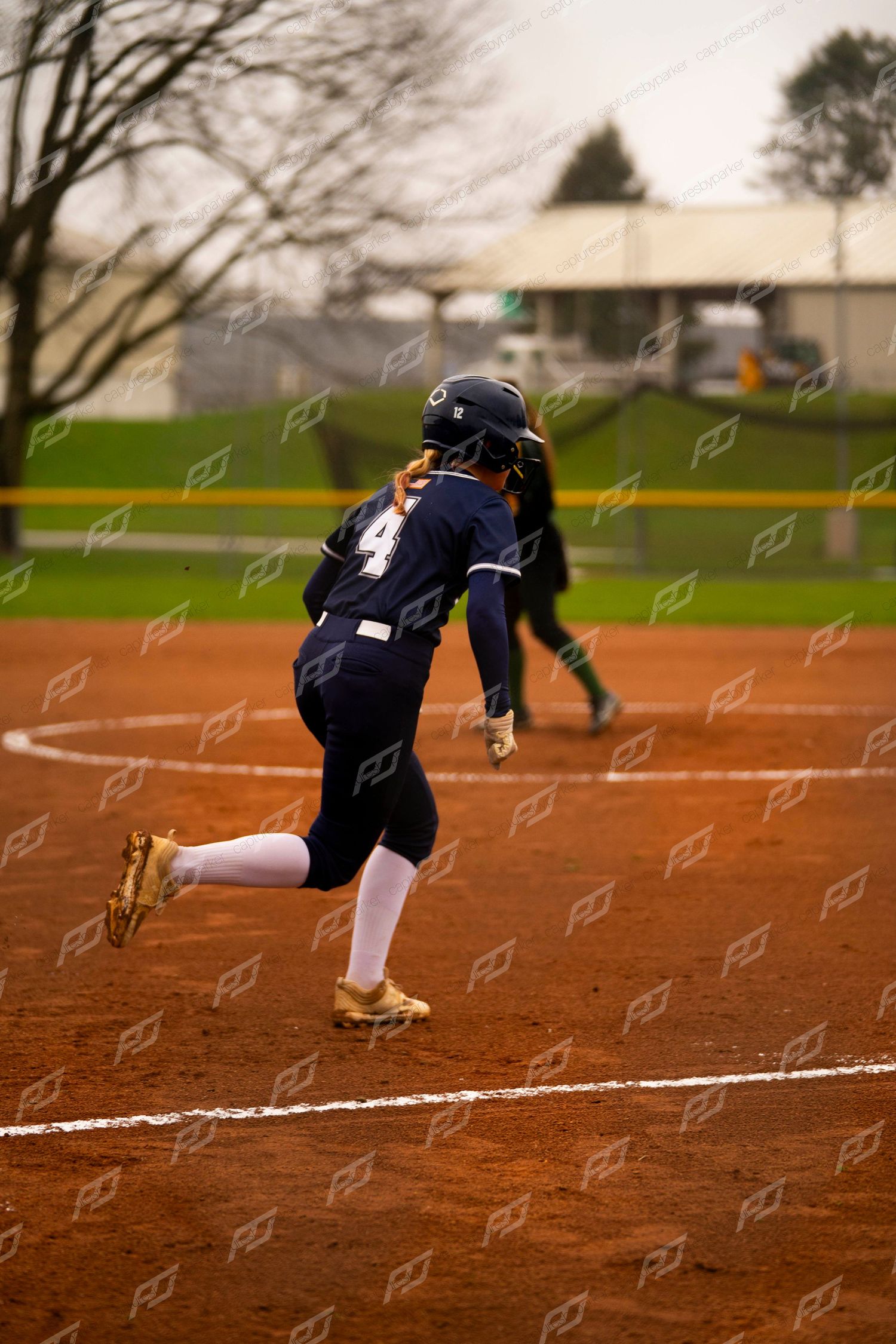 Softball player wearing number 4 in navy uniform sprinting down the baseline after hitting the ball.