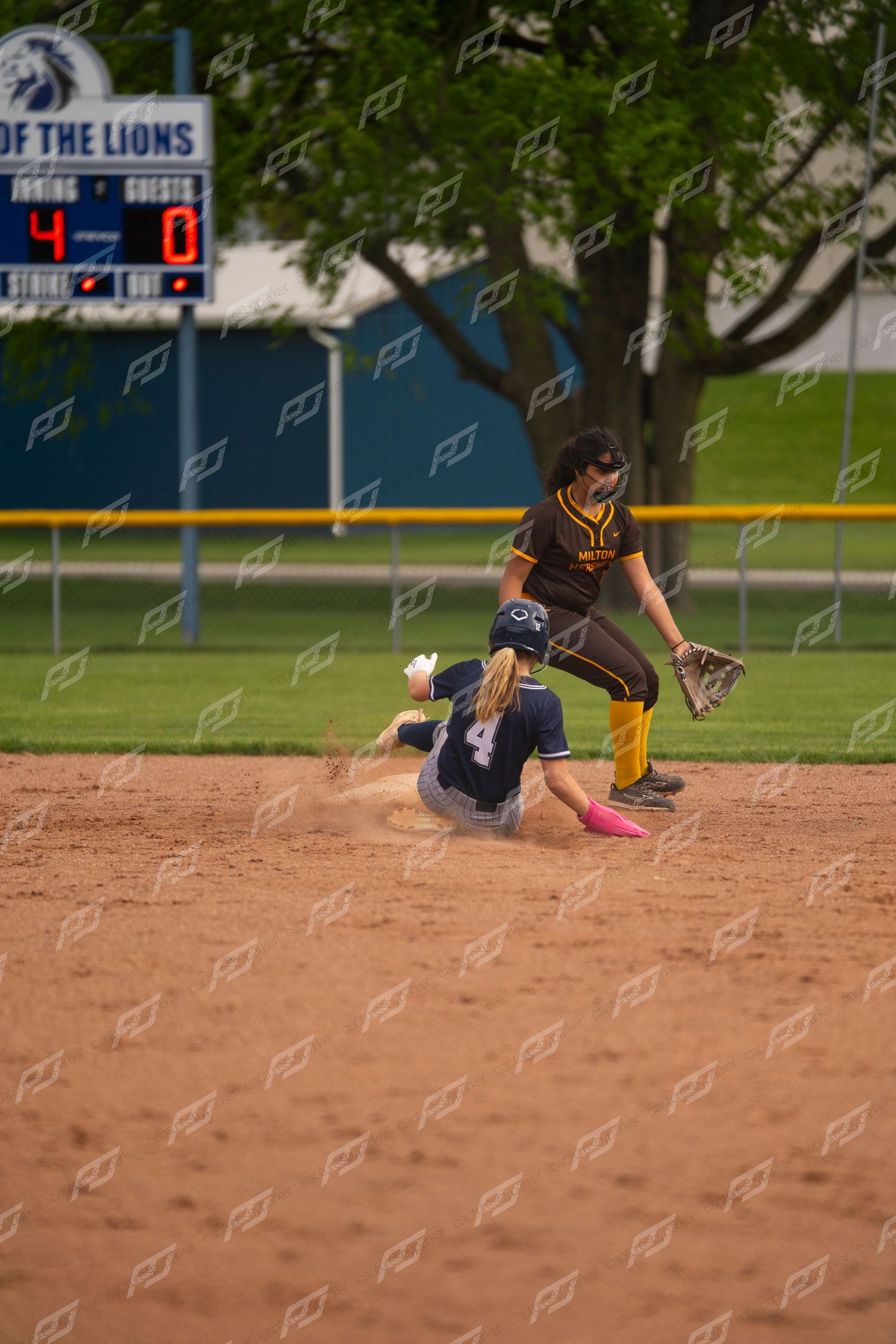 Softball player number 4 slides into second base as the opposing fielder attempts a tag.
