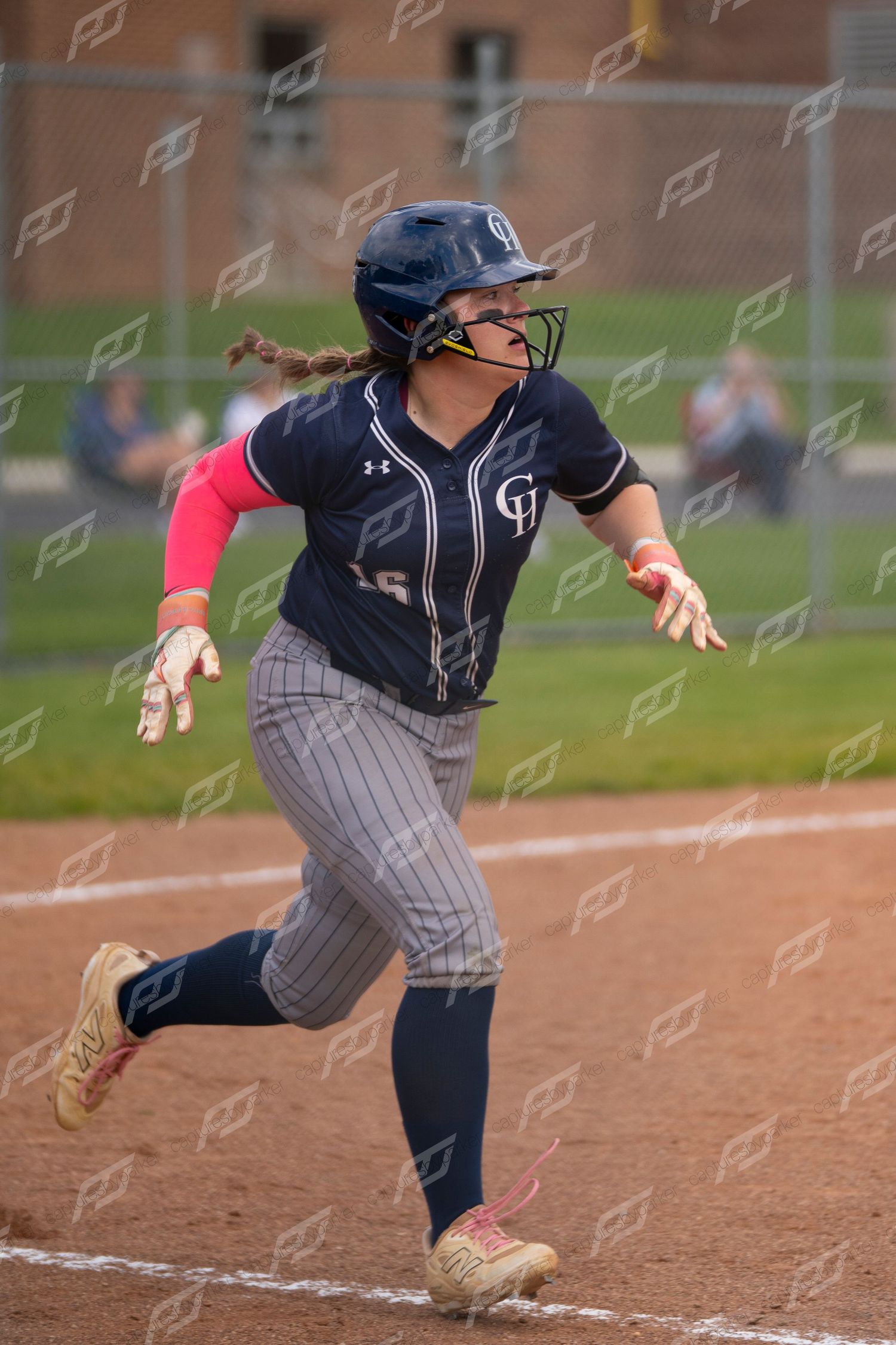 Female softball player in navy uniform sprints toward first base during a competitive game.
