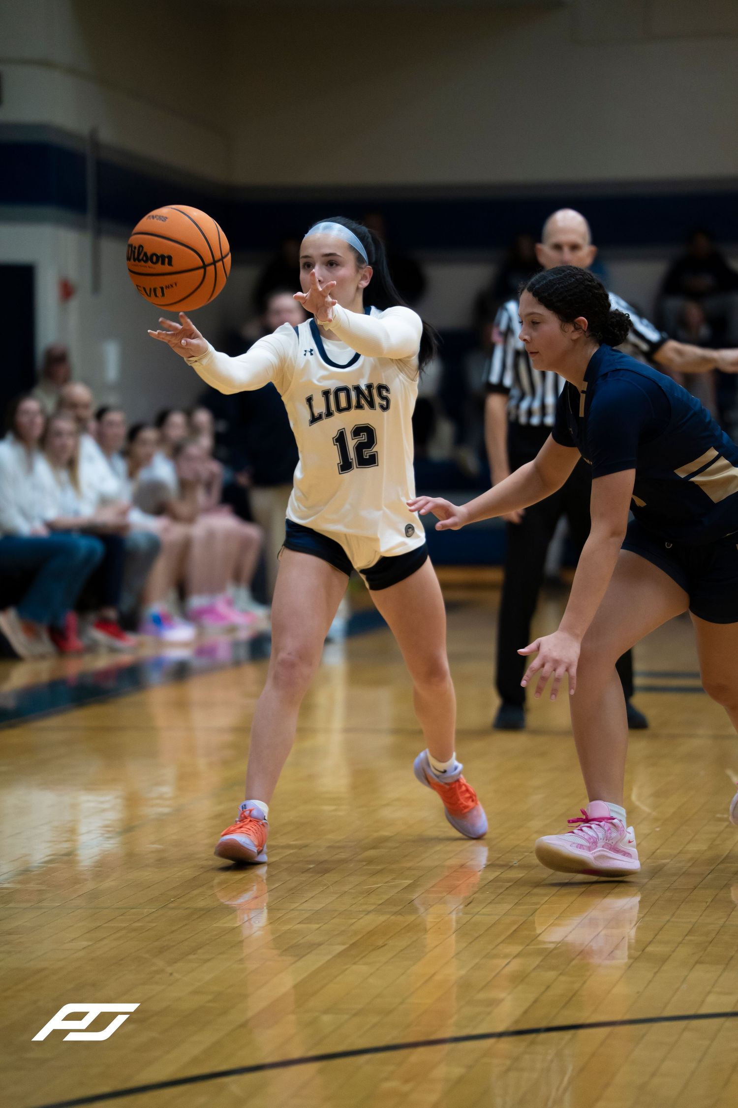Lions number 12 passes the basketball while being defended during a girls basketball game.