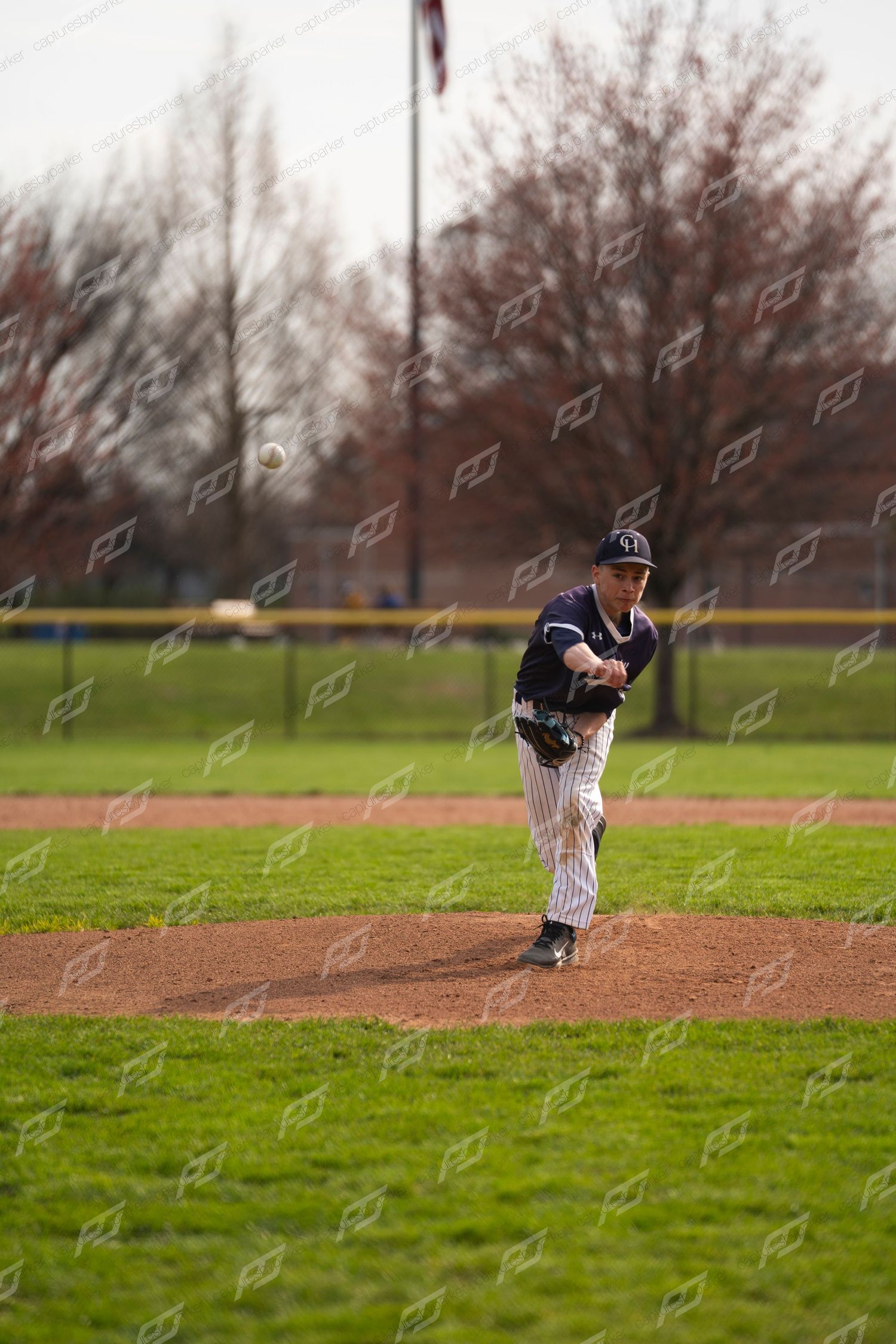 Youth baseball pitcher in navy pinstripe uniform following through on a pitch during a spring season game.
