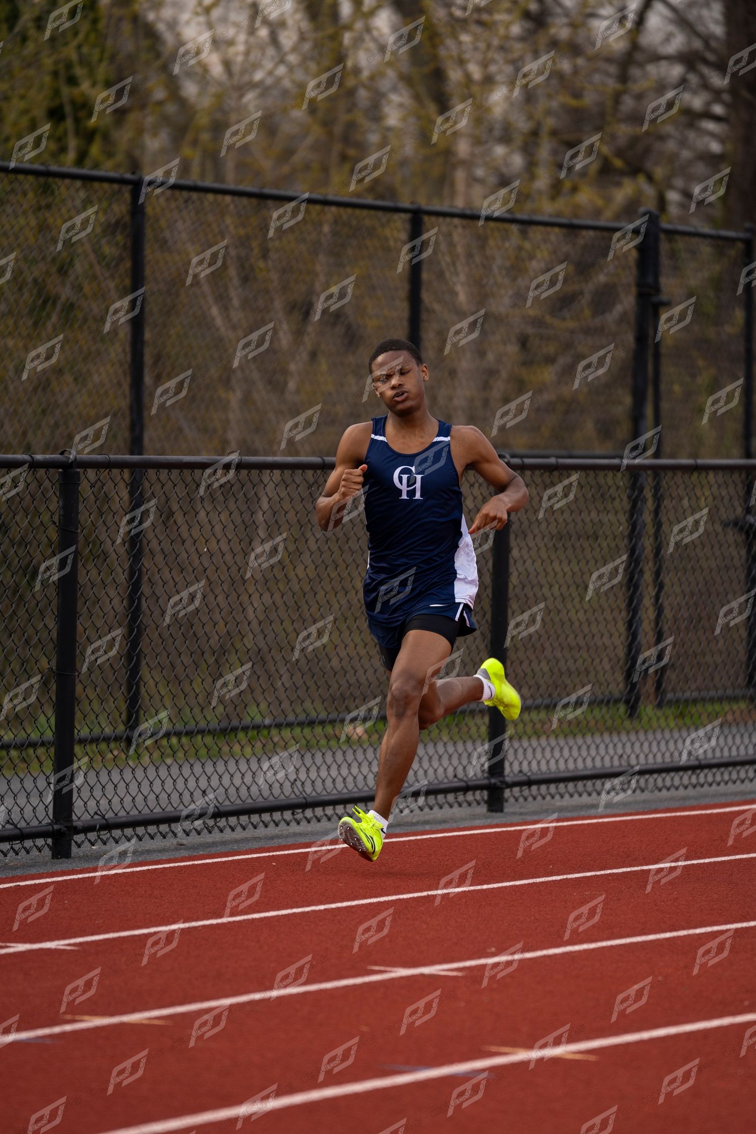 Male track athlete in navy uniform sprints on red track during competition.