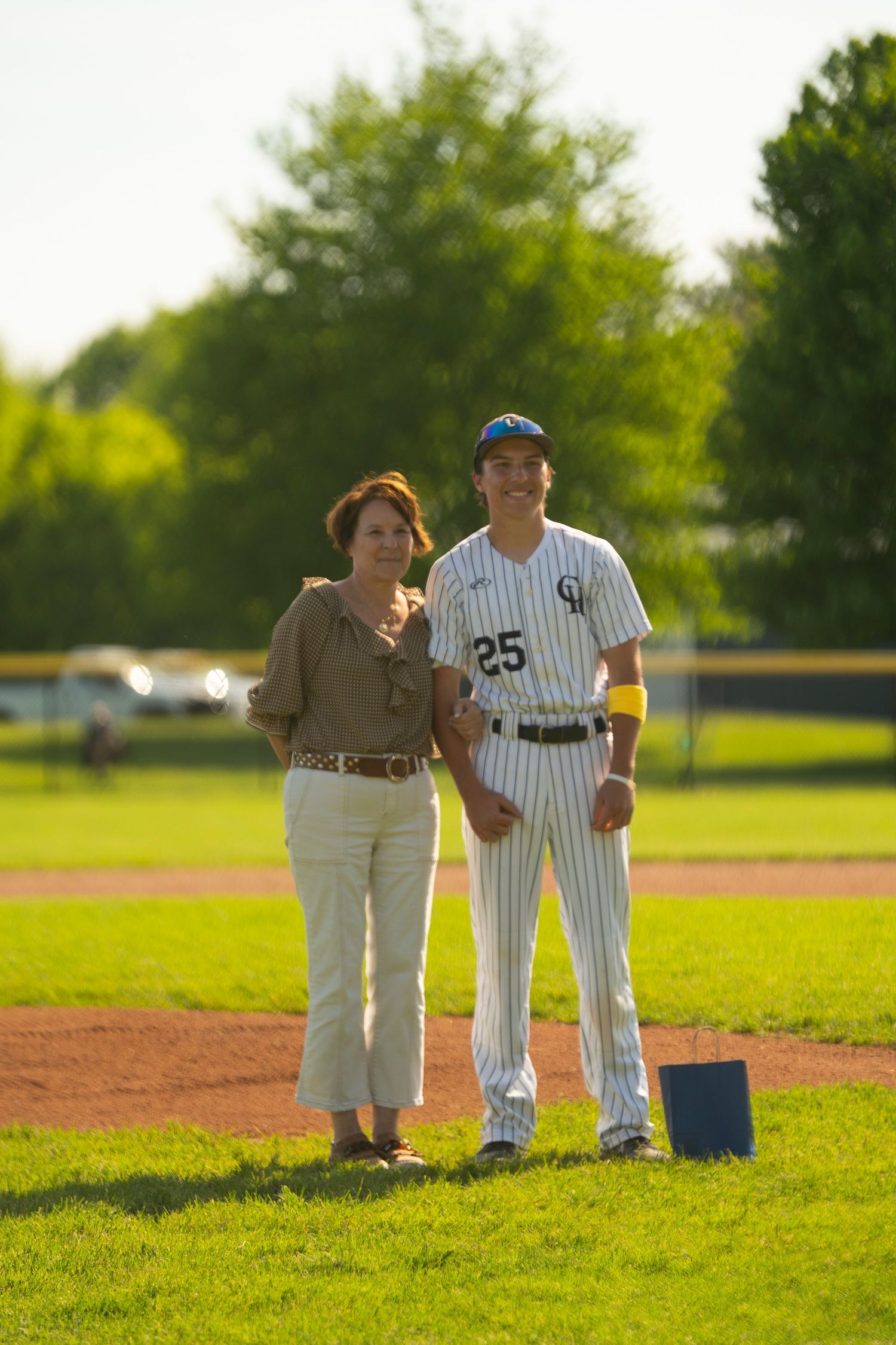 Baseball player #25 in pinstripe uniform stands with a woman smiling on a sunny green baseball field.