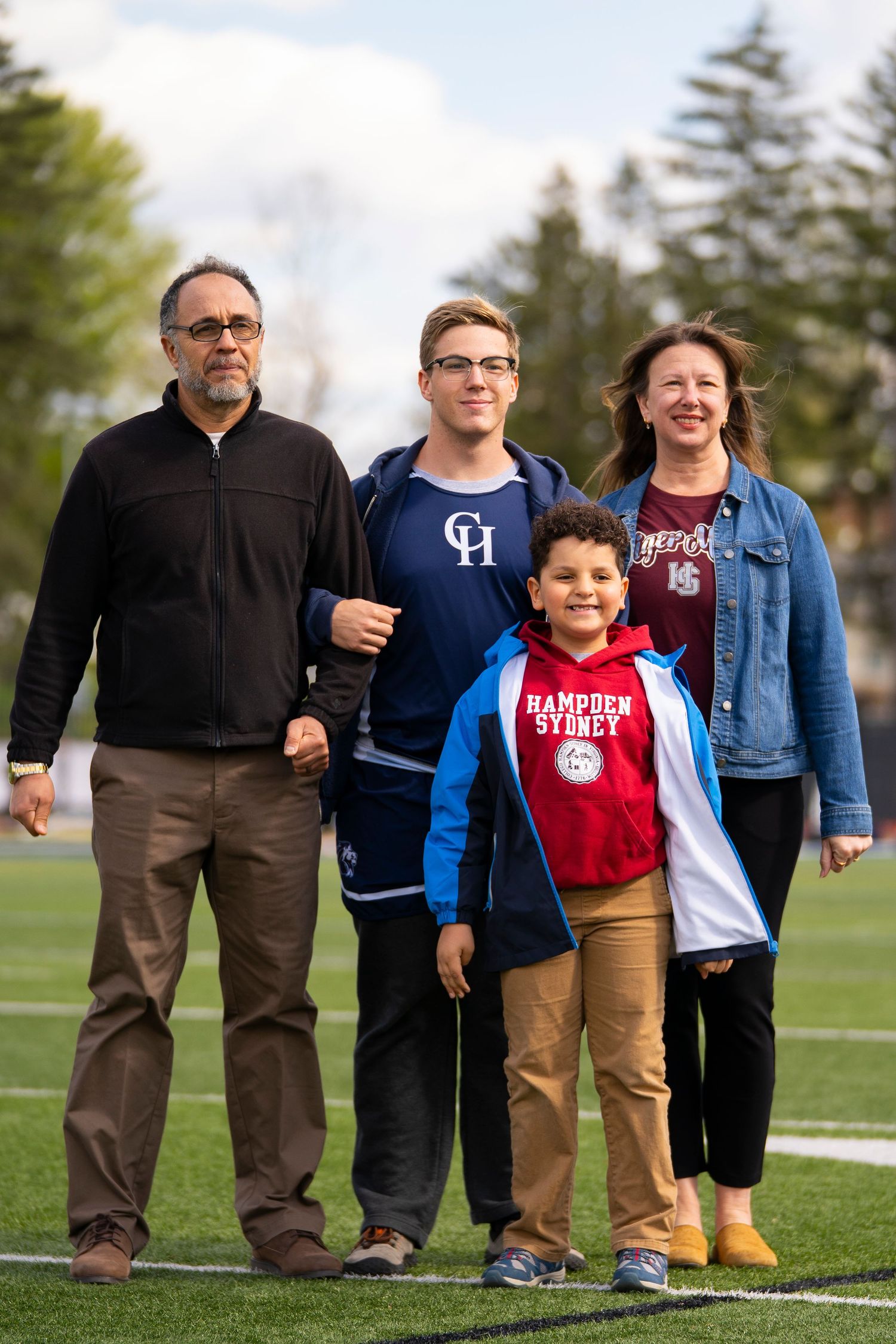 A family of four poses together on a football field during a school senior day event.
