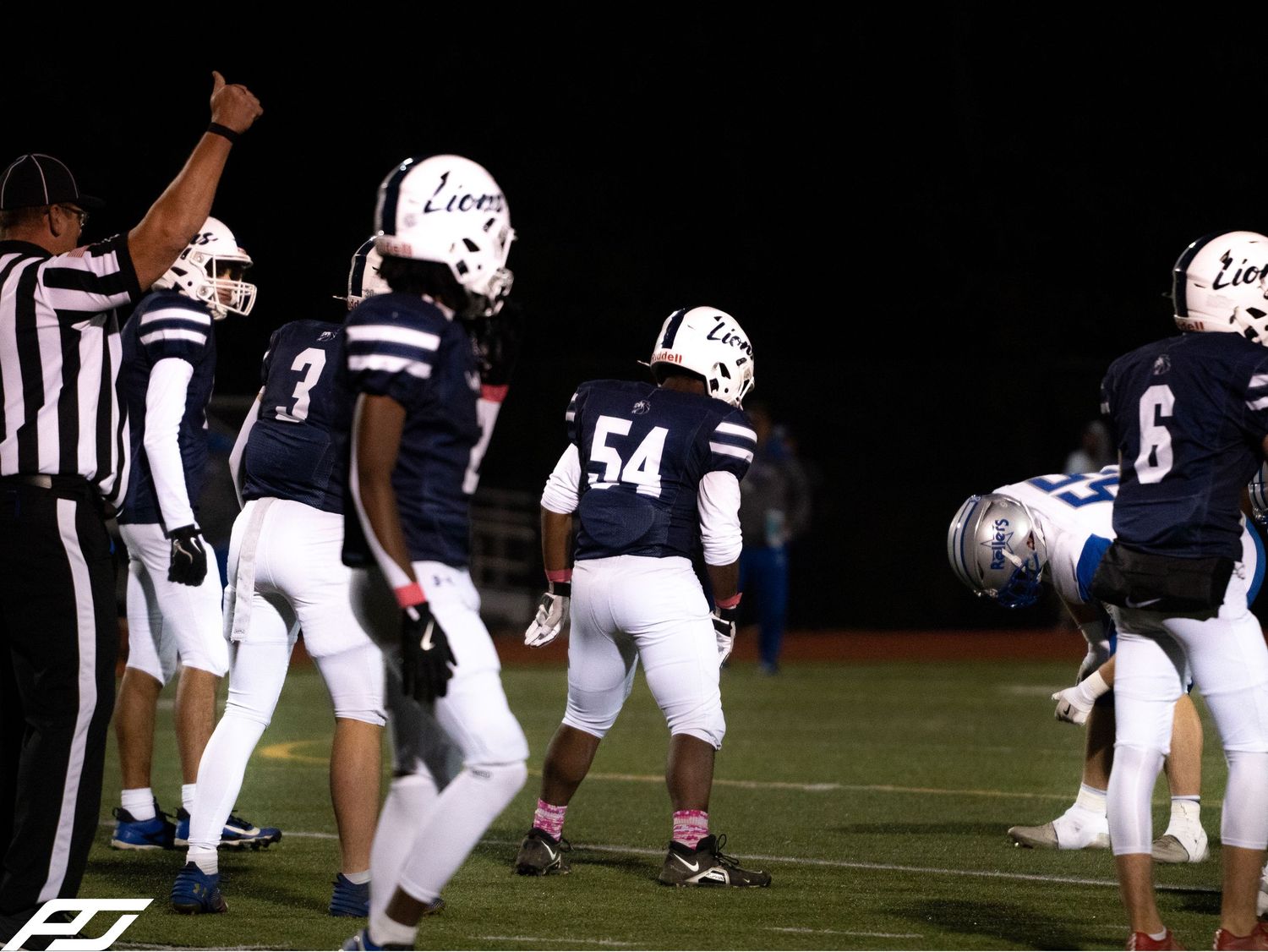 Football referee signals first down as Lions team players in navy uniforms celebrate on night field.