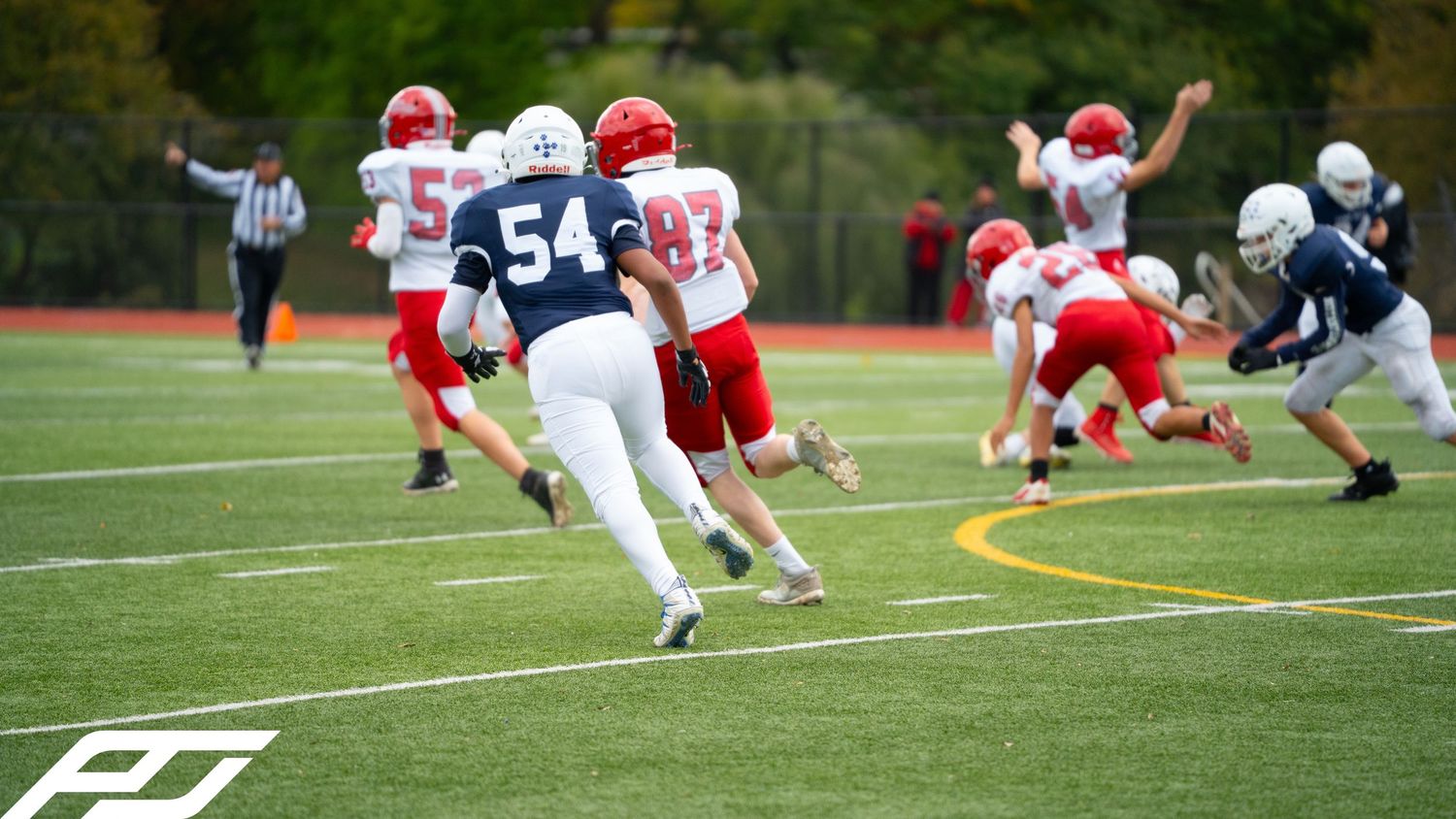 Youth football players in red and navy uniforms compete during an outdoor game.