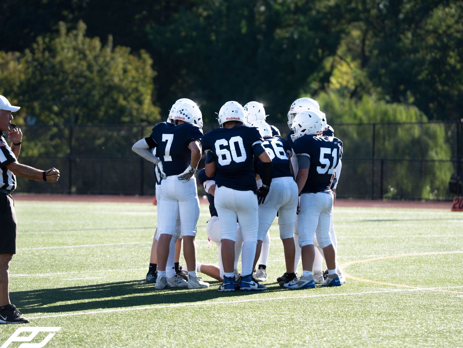 Youth football team huddles together on the field during a Camp Hill game.