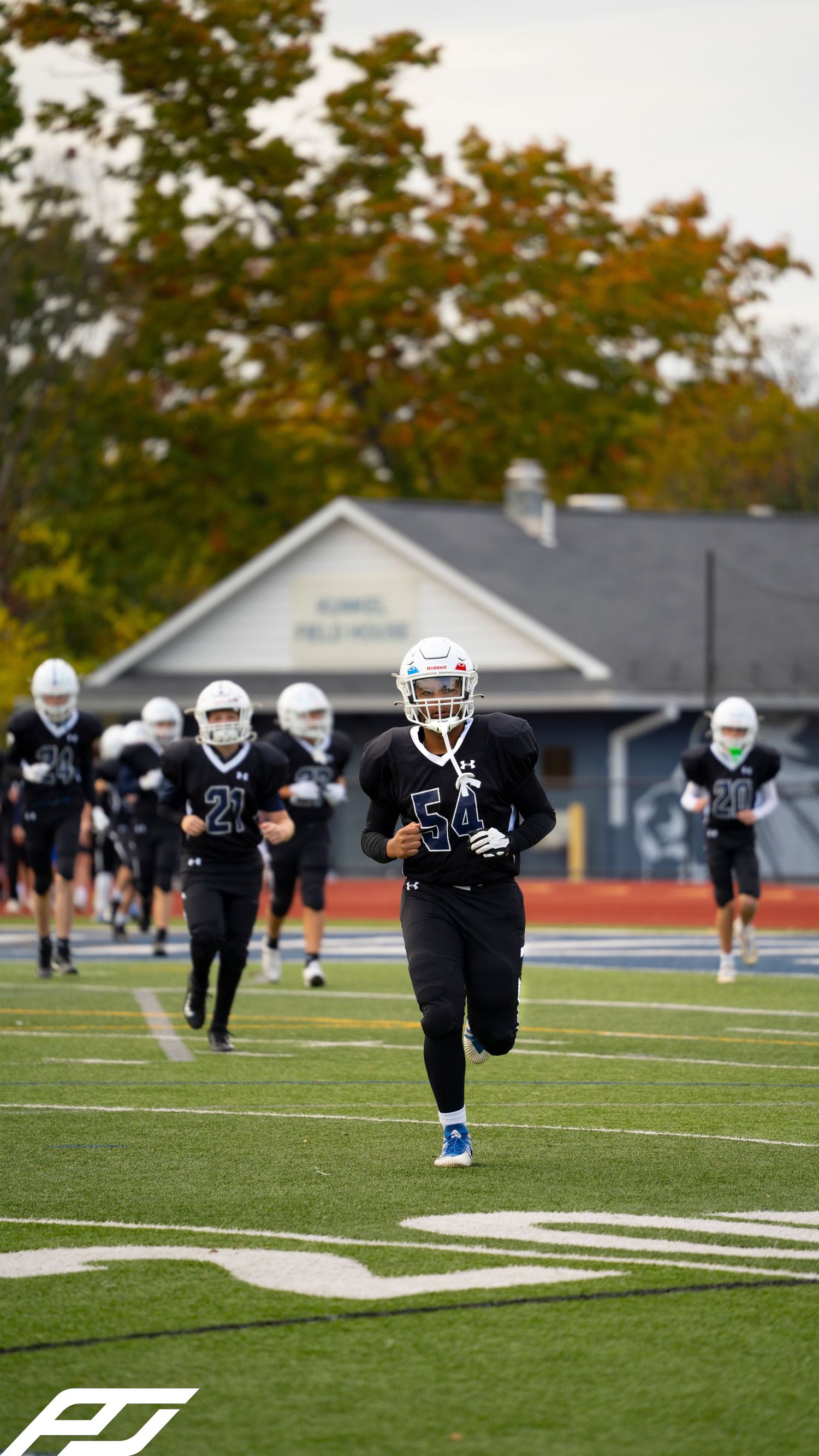 Youth football team in black uniforms runs onto field led by player #54.