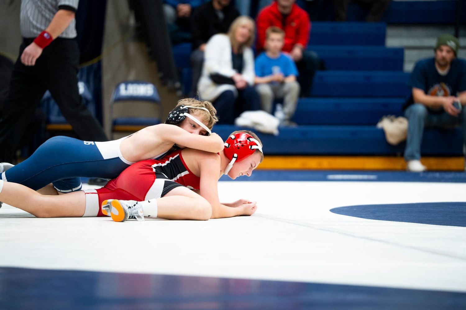 High school wrestler in blue pins opponent in red singlet to the mat during a wrestling match.