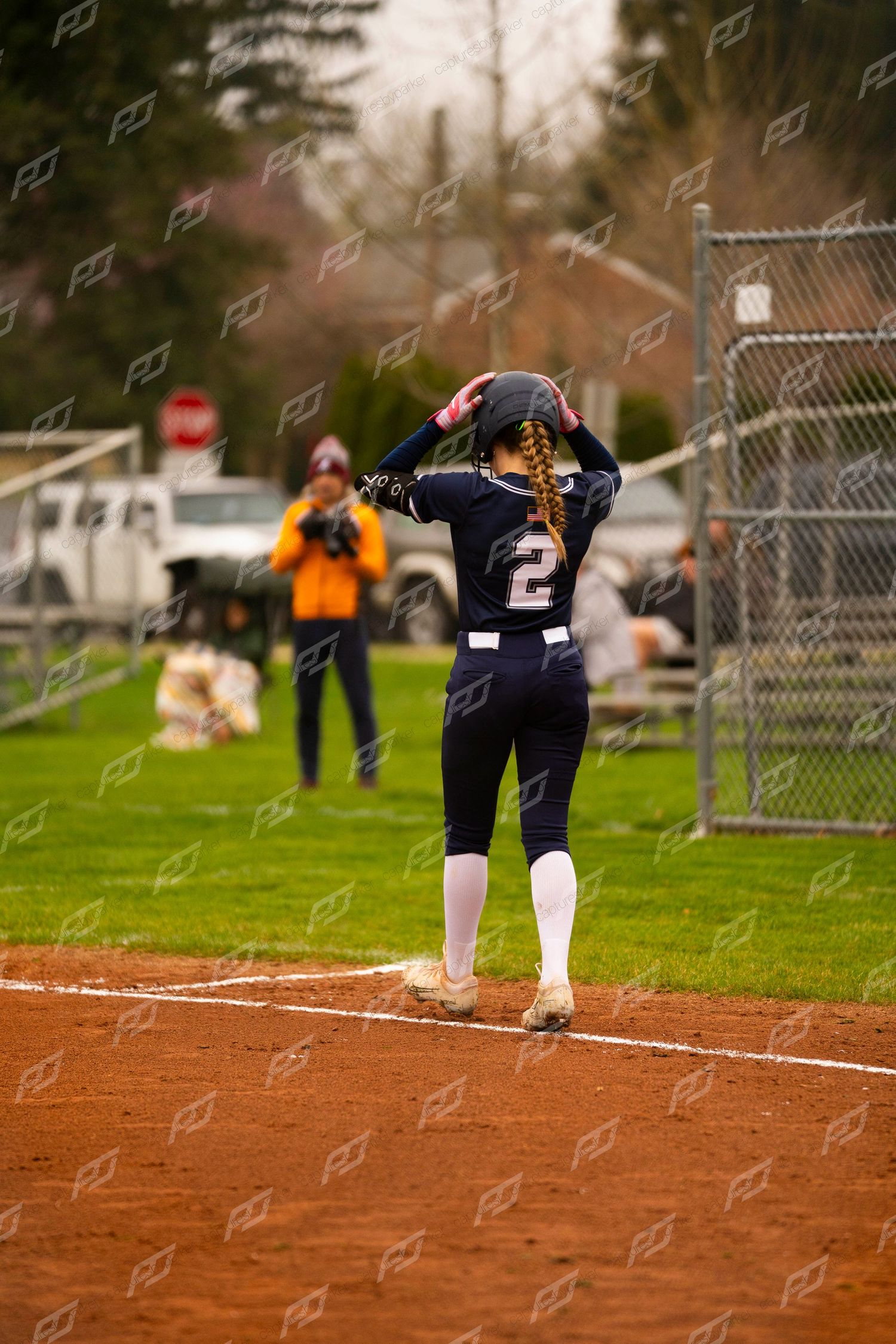 Softball player number 2 in navy uniform stands at base holding her helmet.