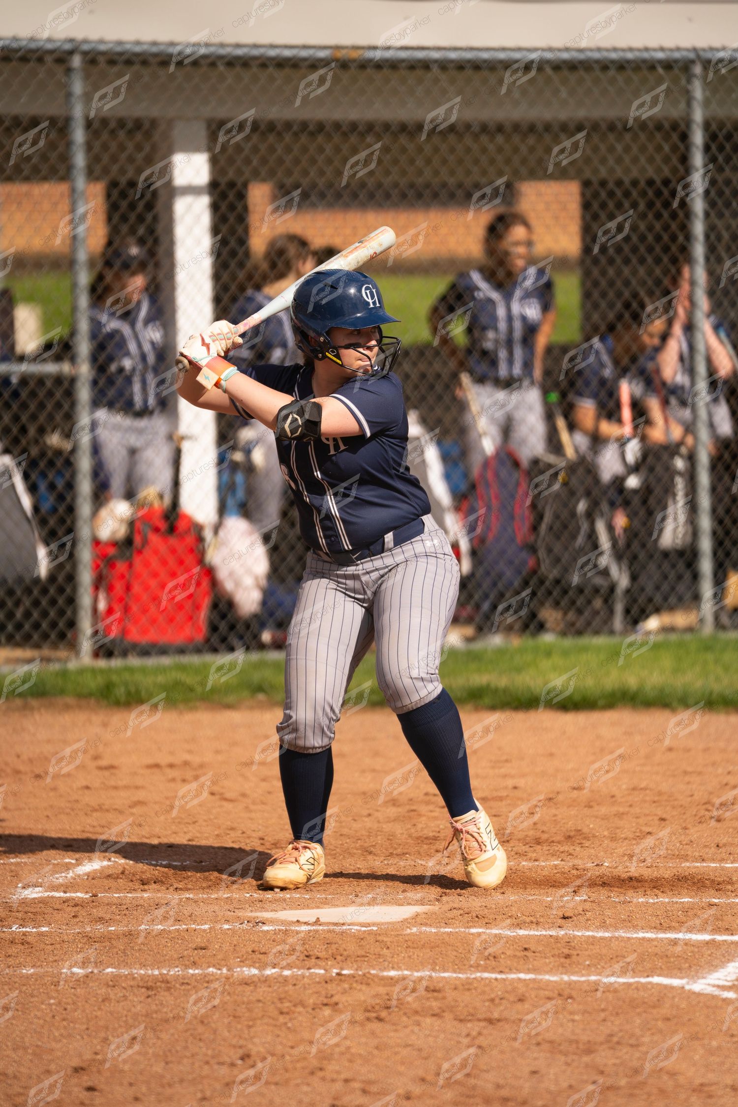 Female softball batter in navy pinstripe uniform stands ready at plate during outdoor game.